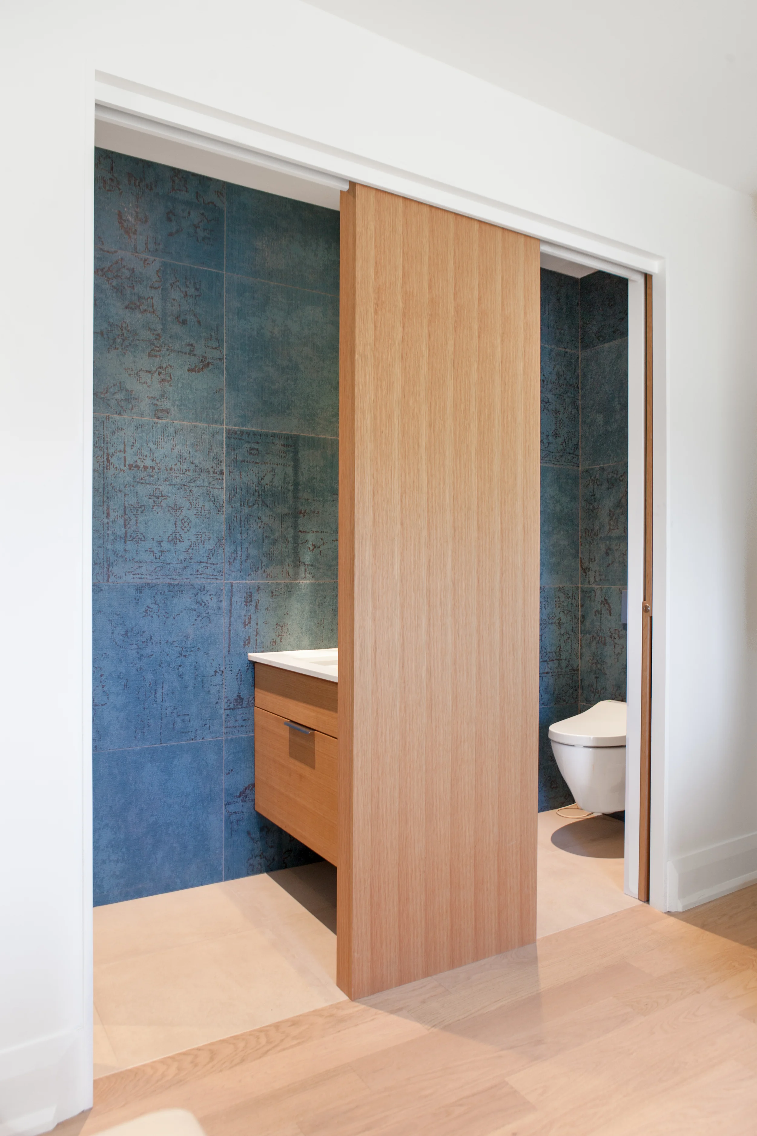When opened, the pocket doors reveal a vibrant blue wall tile that evokes a rich tapestry, and appears to runs continuously through both rooms of the ensuite.
