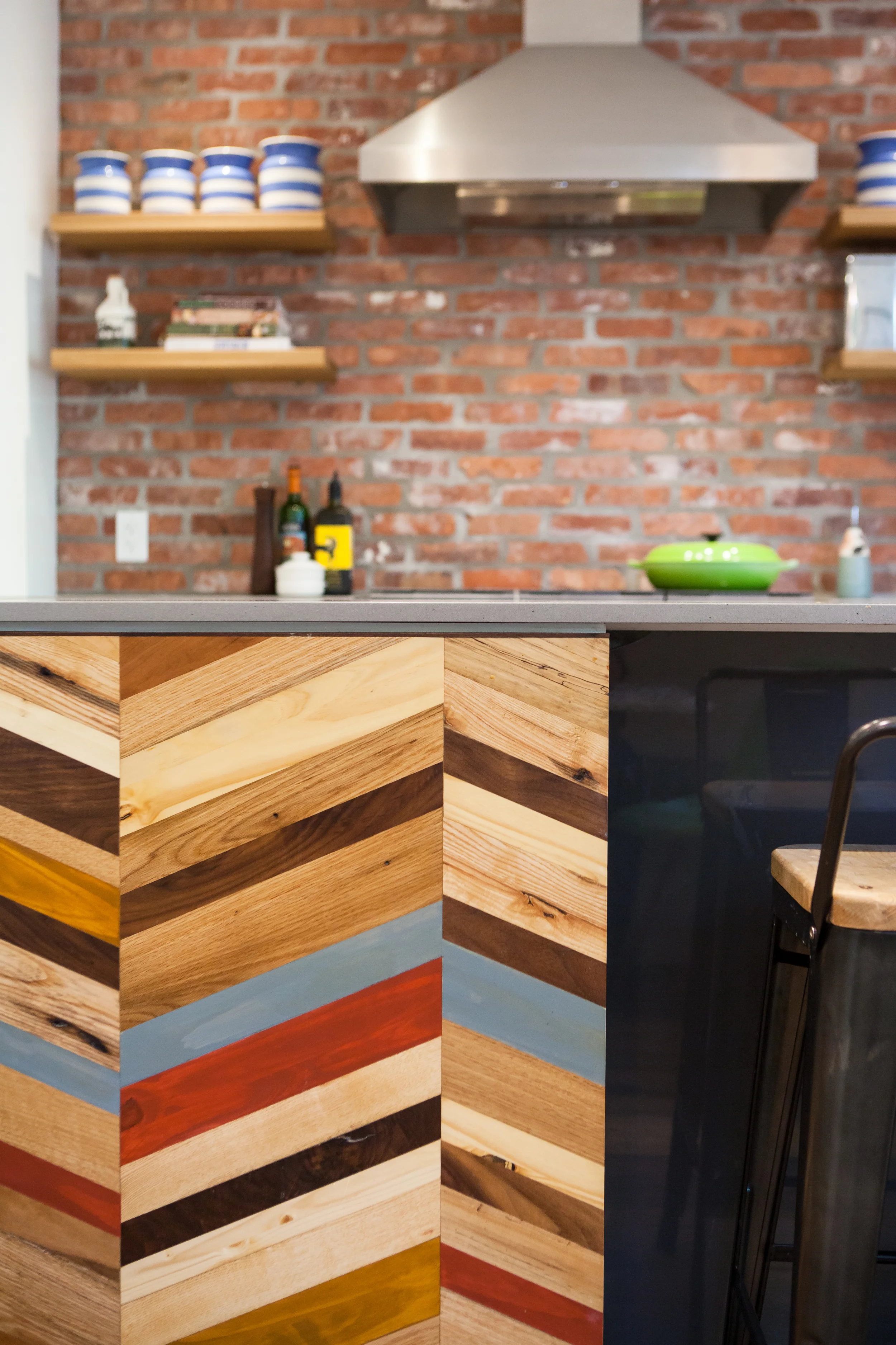 The back of the island features a bold custom panel that combines various reclaimed woods into a graphic, chevron pattern.