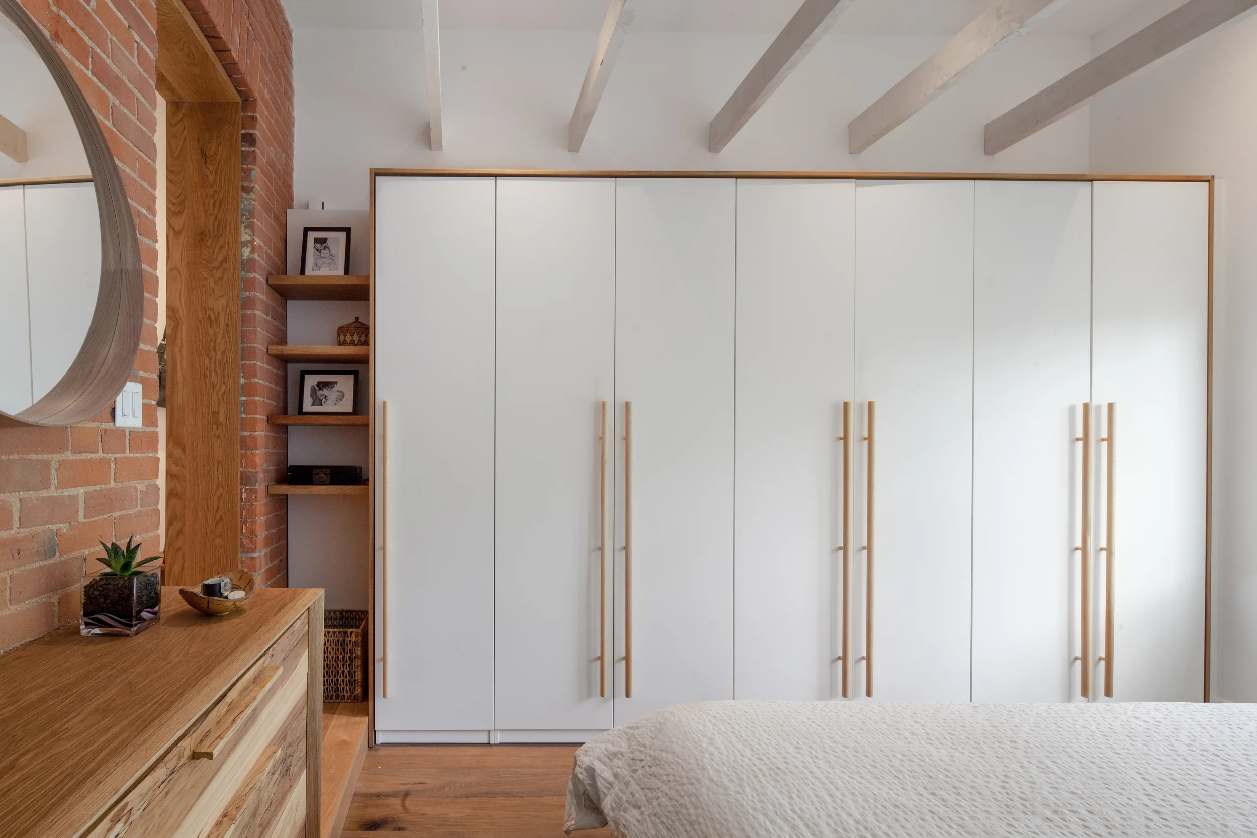 A wall of closets is considered as part of a composition that relates to open shelves and a custom oak step at the entry threshold of the master bedroom.