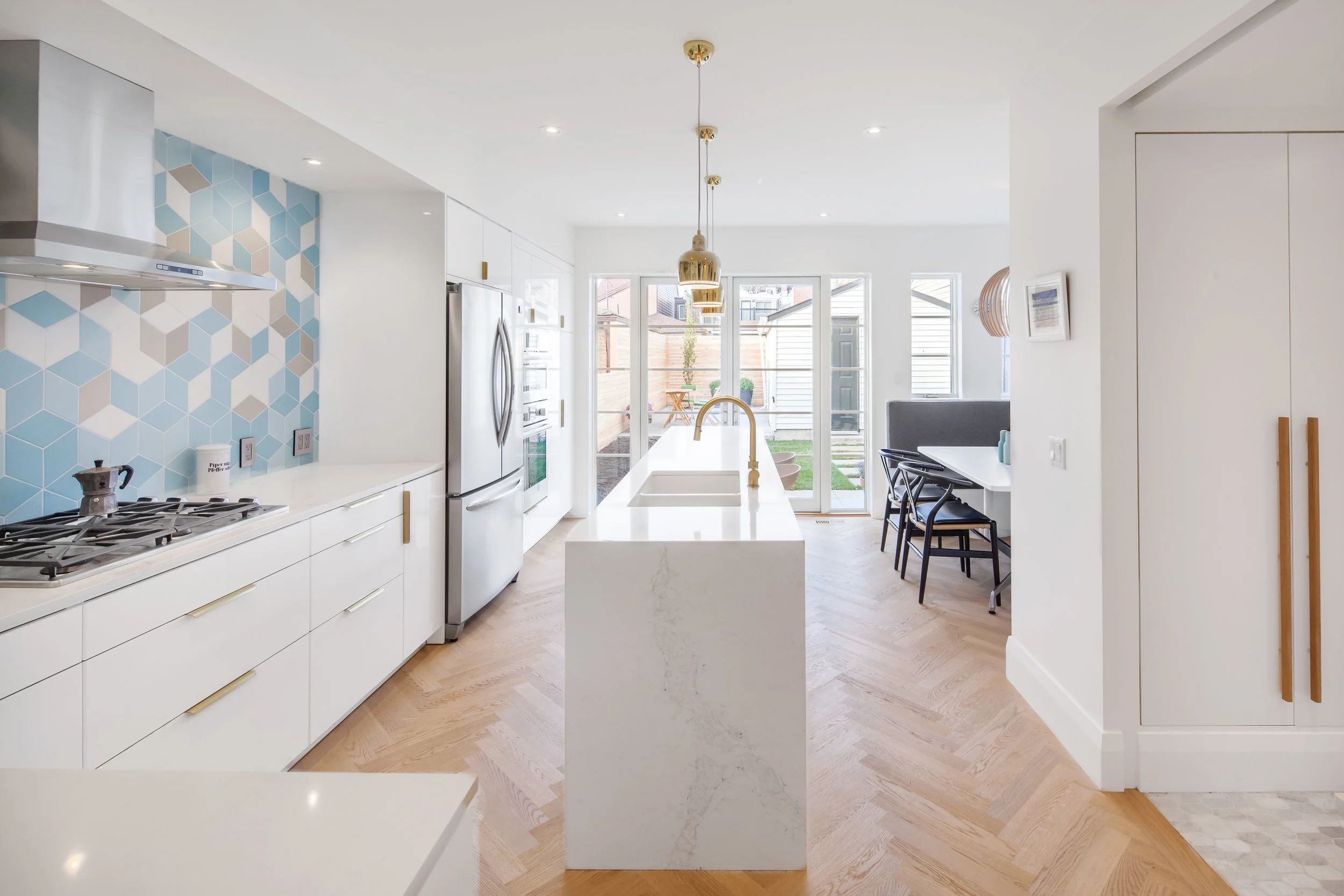The kitchen is designed to become the heart of the home, looking out over the backyard. White oak flooring set in a herringbone pattern, and a bold, geometric blue backsplash tile are the big moves that bring texture and colour into the space, providing visual interest without overpowering the fresh, bright and light palette.