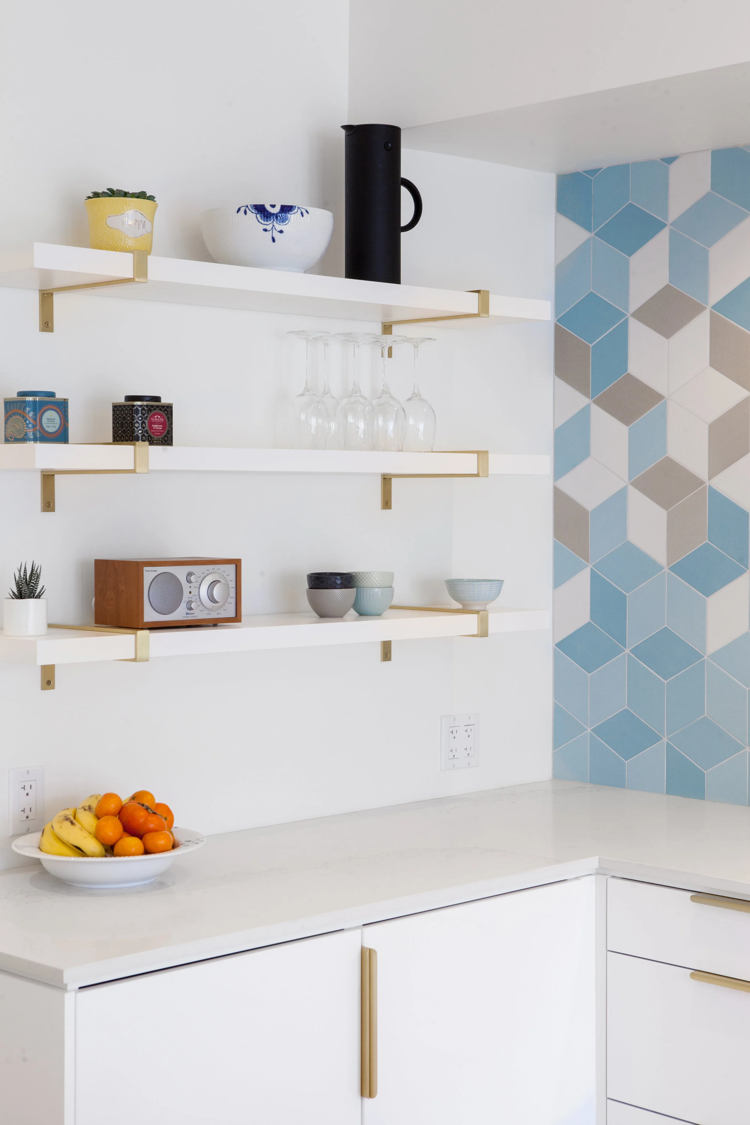 Custom brass brackets support open shelves for glassware and ceramics.