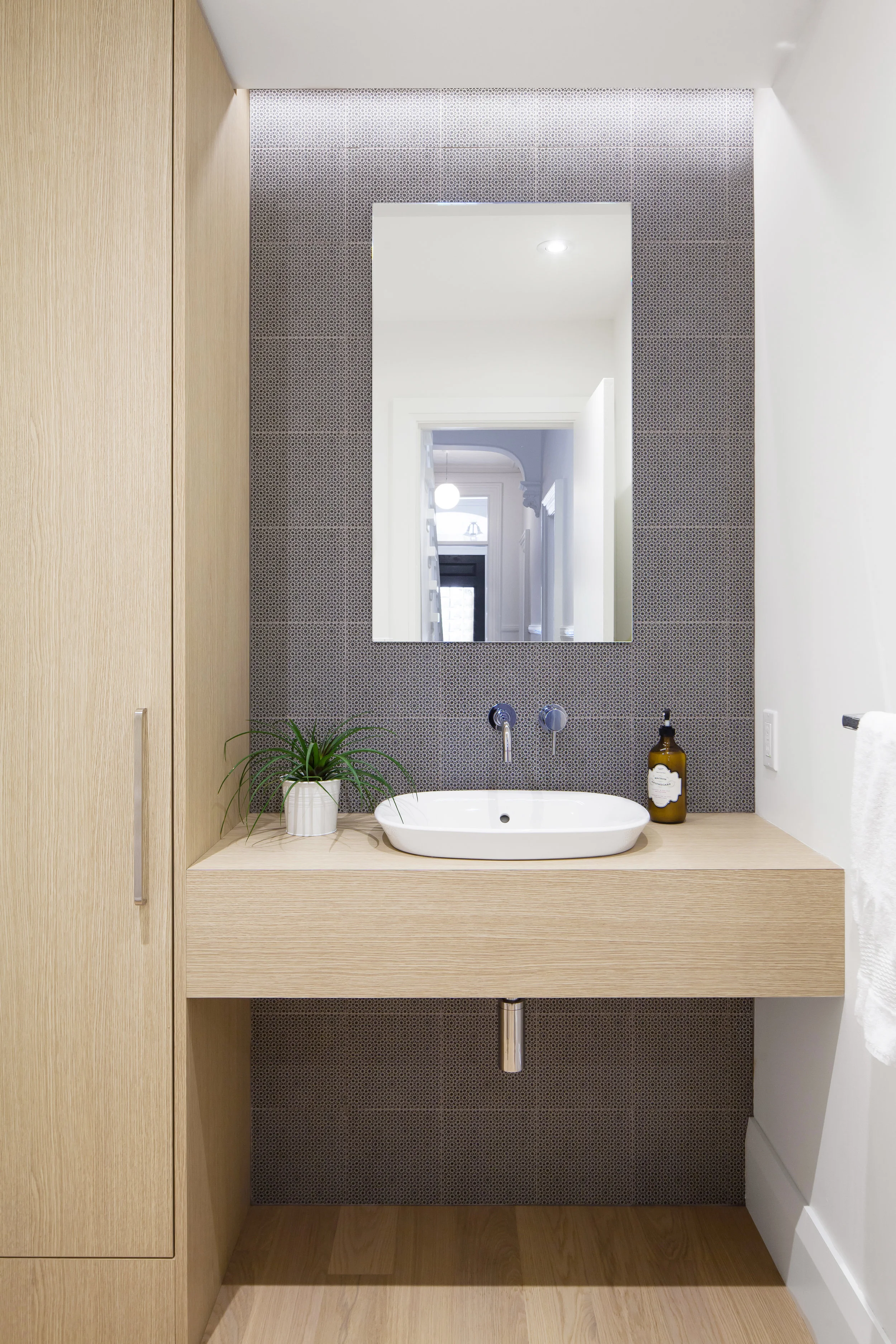 The powder room is a thoughtfully composition of light wood closet and vanity top, set against an intricate blue tile that is illiuminated from above by a hidden cove light.
