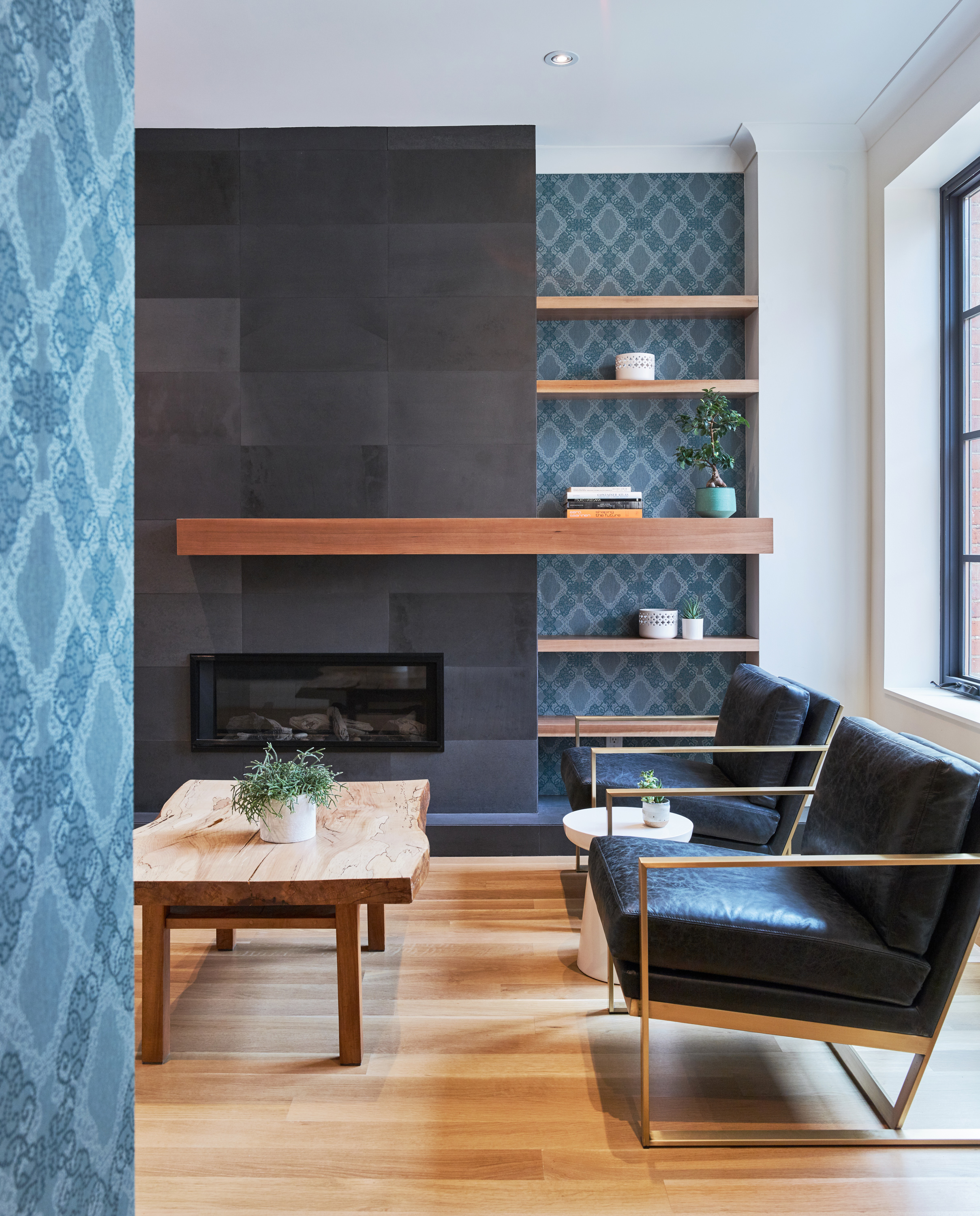 The black tile surround on the fireplace offsets the natural wood floating shelves and mantle, while allowing the blue wall covering to stand out.