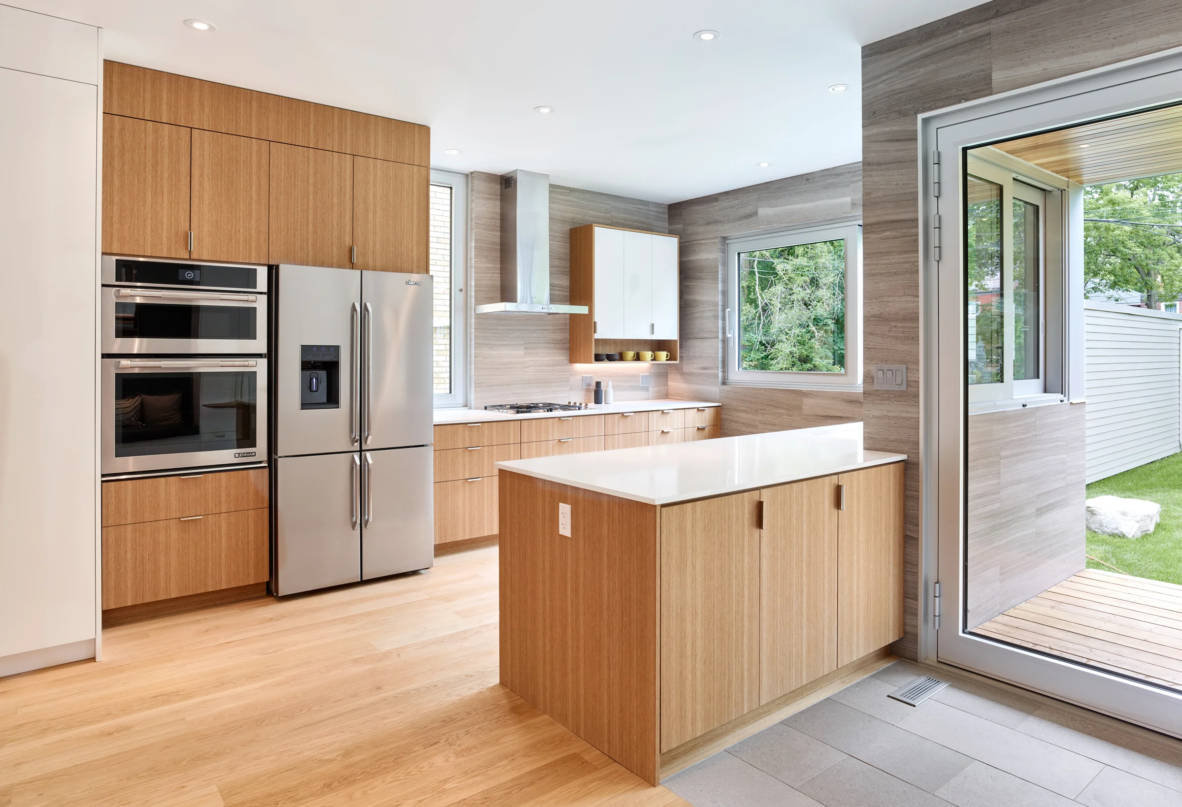 The kitchen overlooks the rear yard and features sliding windows that allow it to open directly onto the deck and yard. The exterior limestone cladding wraps inside the kitchen as a feature tile and backsplash.