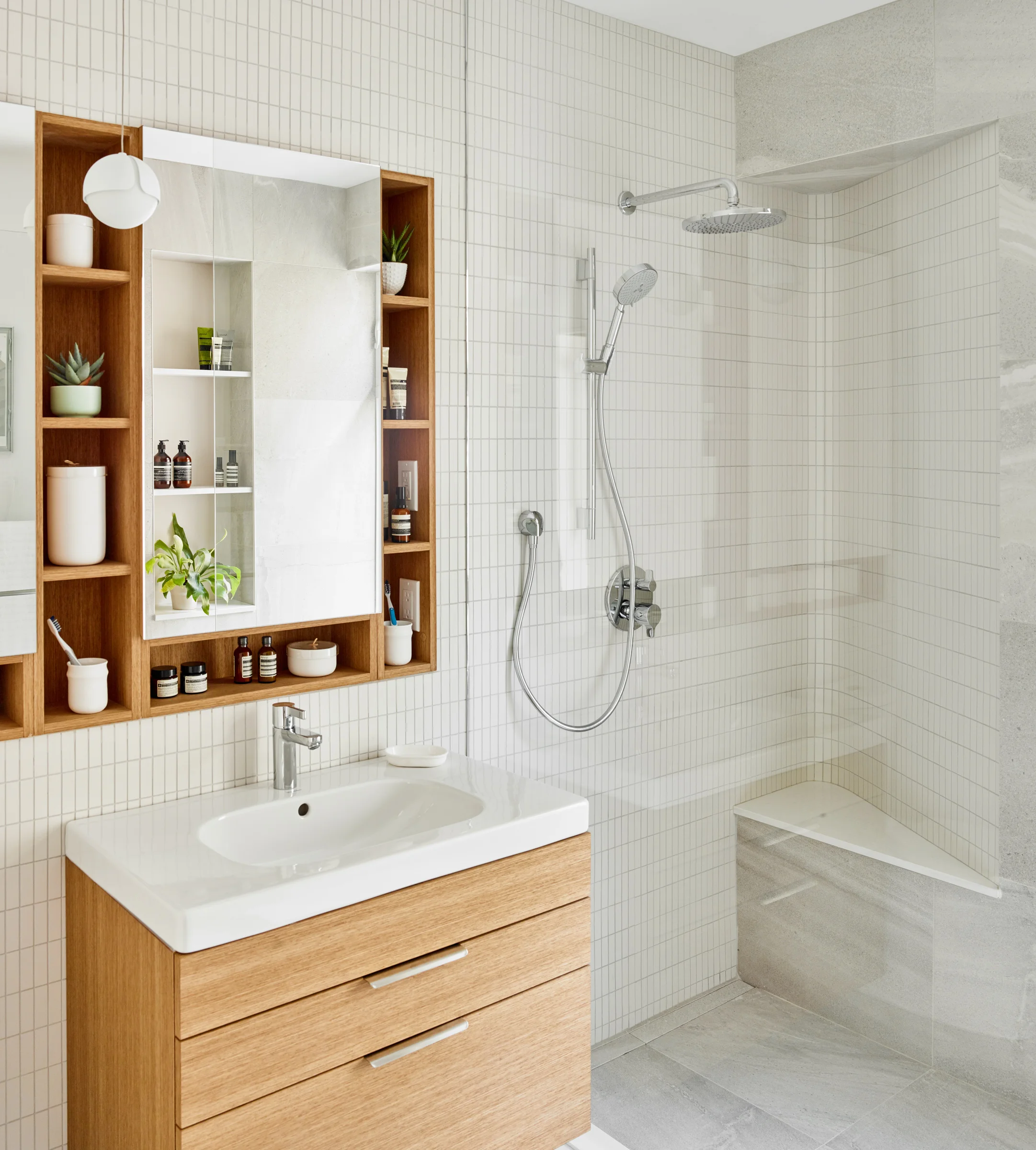 A tiled wall containing inset shelves and a medicine cabinet slides seamlessly into the shower and then curves back to form a discrete bench in the shower.
