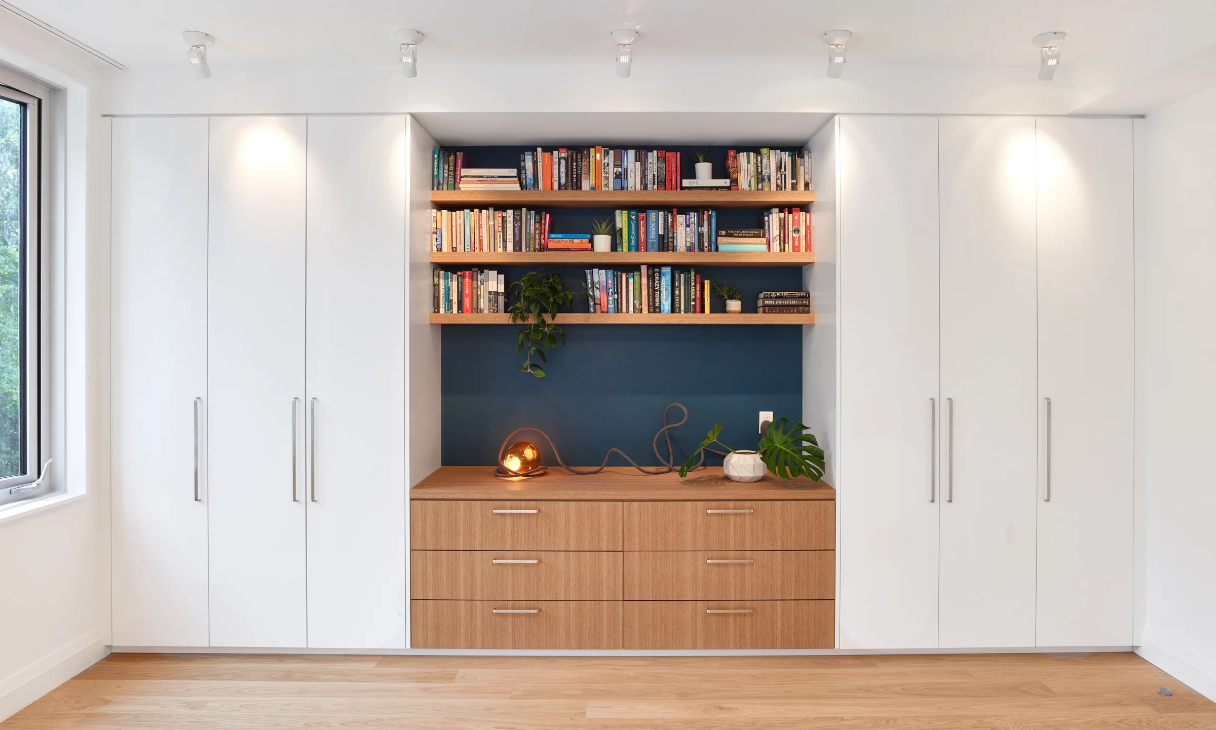 A composition of closets, drawers and bookshelves sits opposite the bed.