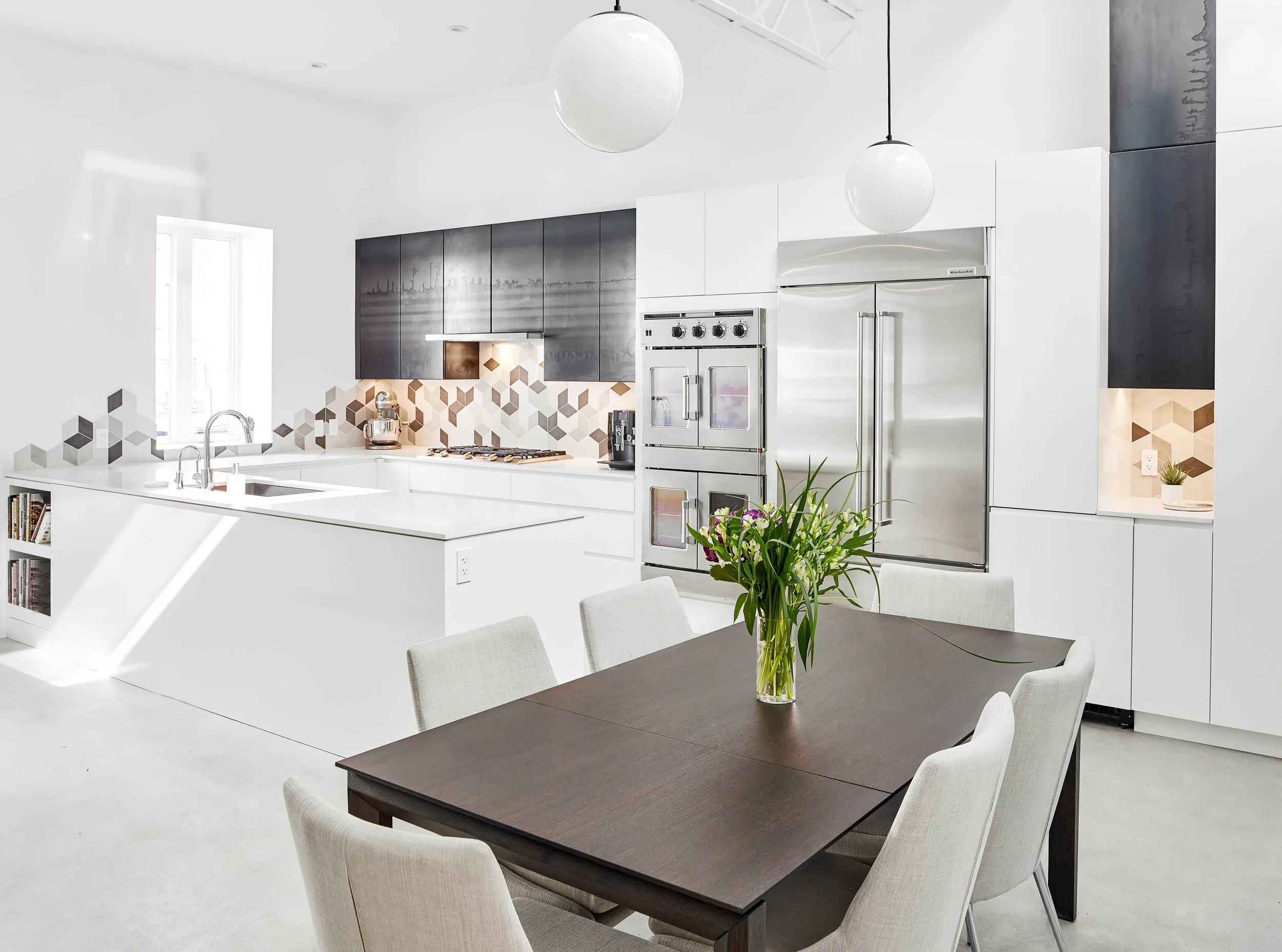 A spacious kitchen is large enough for two to cook at once and features a double wall oven and wide gas cooktop. The geometric backsplash tile organically dissipates along the side wall.