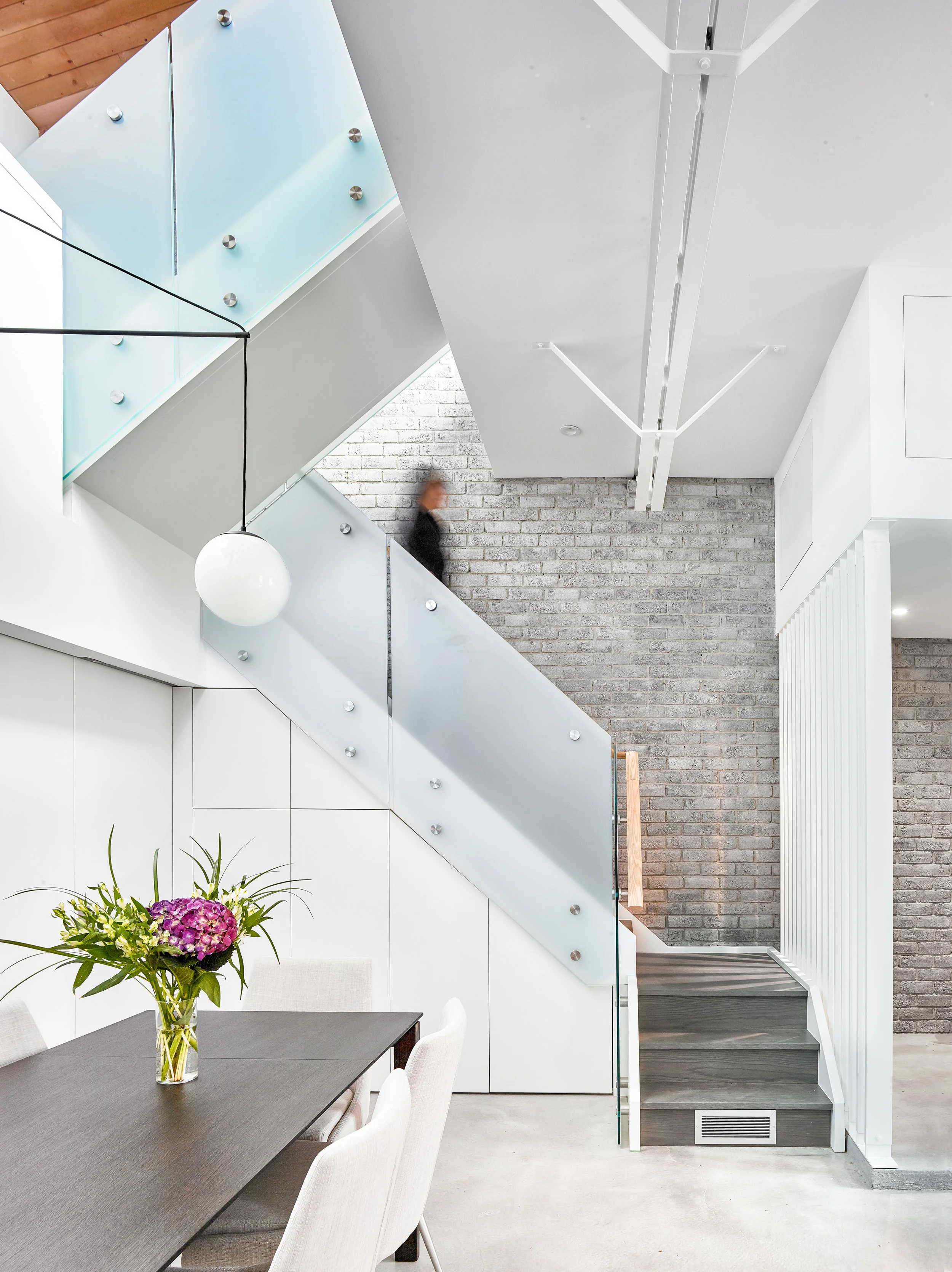 A new stair is divided from the entryway by a wood privacy screen and winds upstairs to the mezzanine, and then further up onto the roof terrace above. The original brick wall is left exposed along this wall and was stained to a soft, muted grey colour. Storage for bikes and luggage is cleverly tucked below the staircase.
