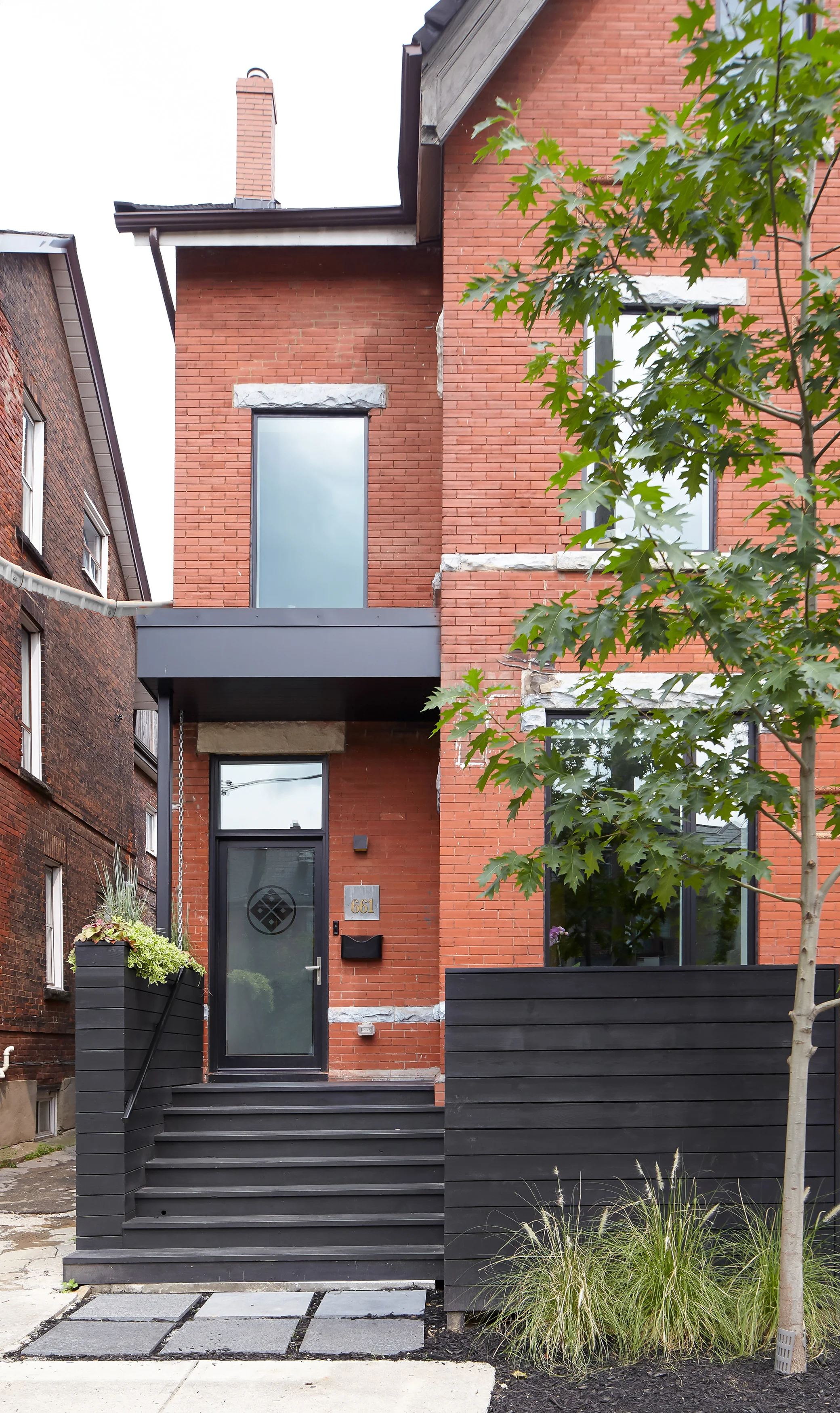 The front porch is rebuilt and tied into wood planters that screen the garbage / relying bins from view.