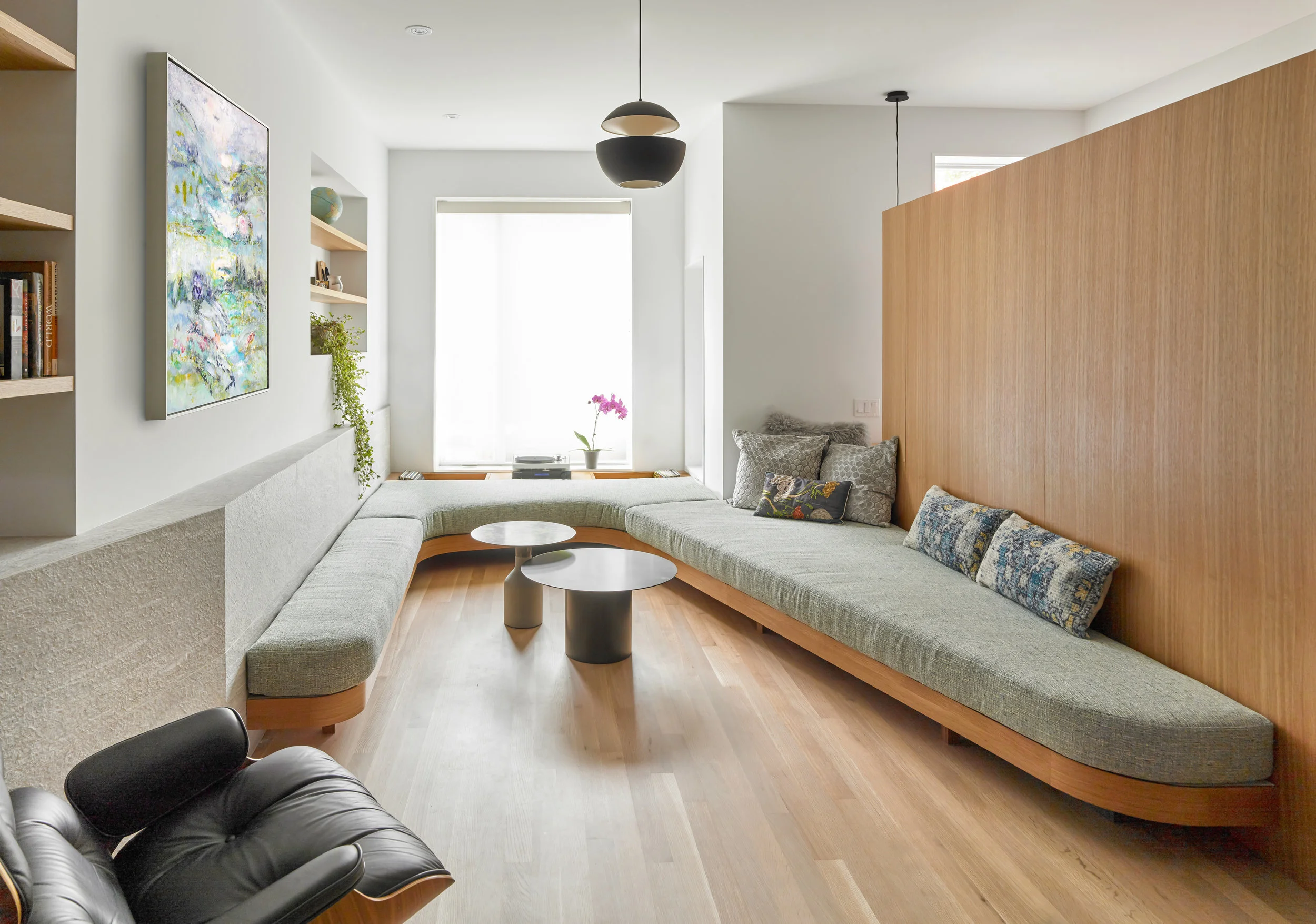 Within a relatively compact living room, a variety of activities are accommodated by a uniquely curved upholstered seat that lines three walls - its depth varies to allow for: conversations, music listening, lounging, reading, napping, etc.