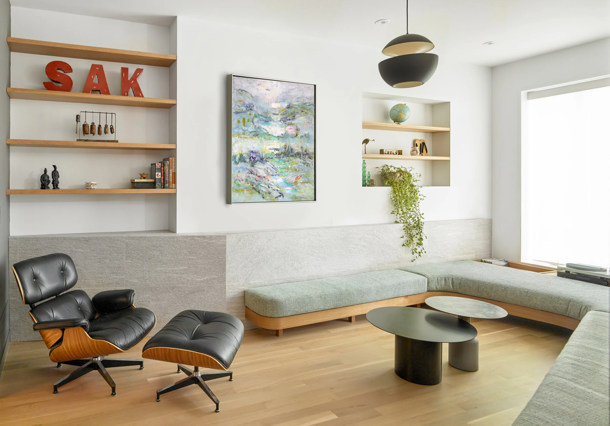 The living room is flooded with natural light. Carefully curated floating shelves display a collection of objects within two niches carved from the wall.