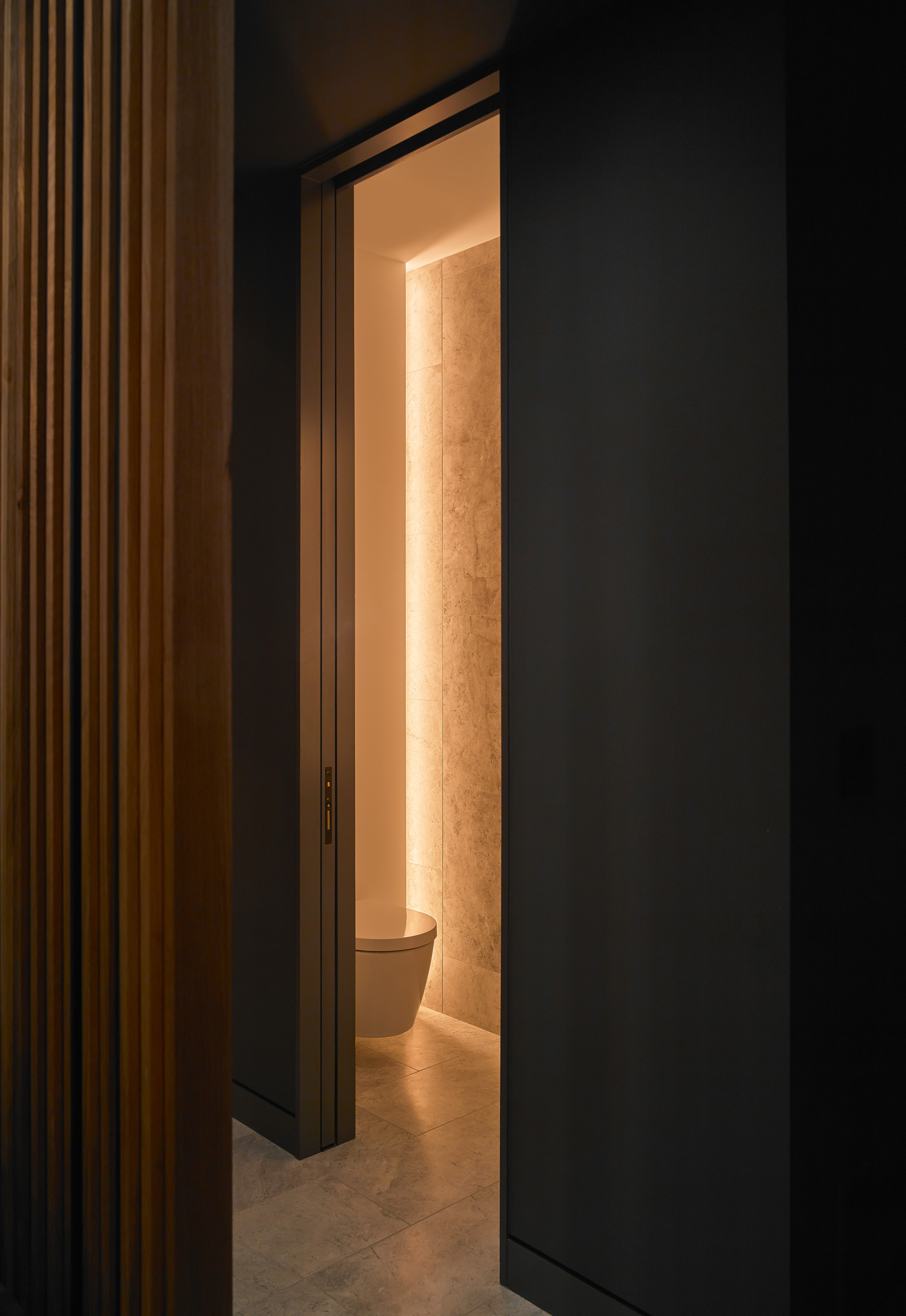The powder room is tucked beside the stairs, and lit with hidden cove lights, meant to give a warm, soft glow. The floor tile that folds up the wall, washed with a warm glow it becomes an architectural night-light as you head up to bed.