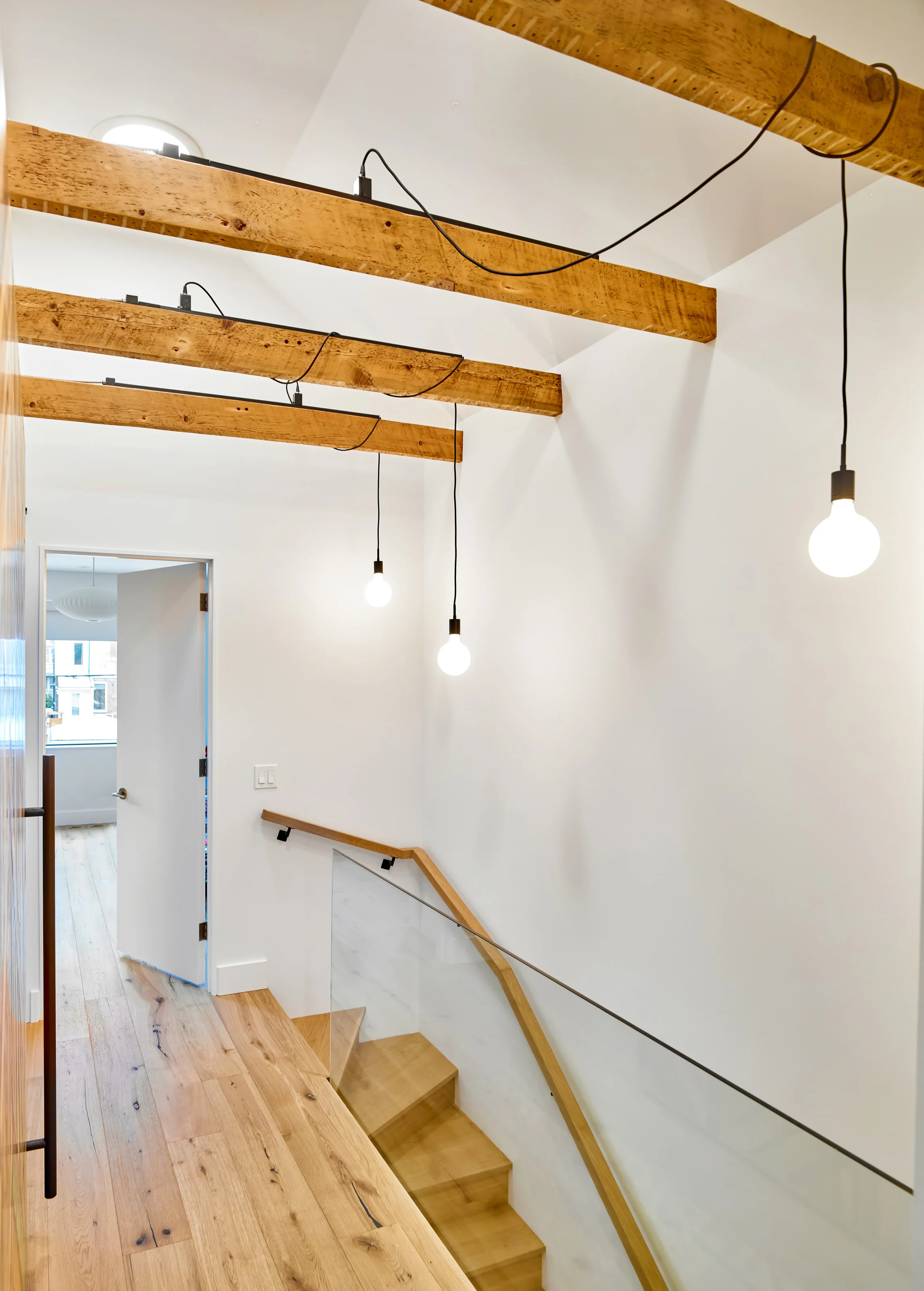 Through the upstairs corridor, a selection of the original ceiling joists are retained and exposed. The ceiling above vaults to a peak and is punctured by three sun tunnels that flood the corridor with natural light. Pendants are precisely dangled between the exposed joists.