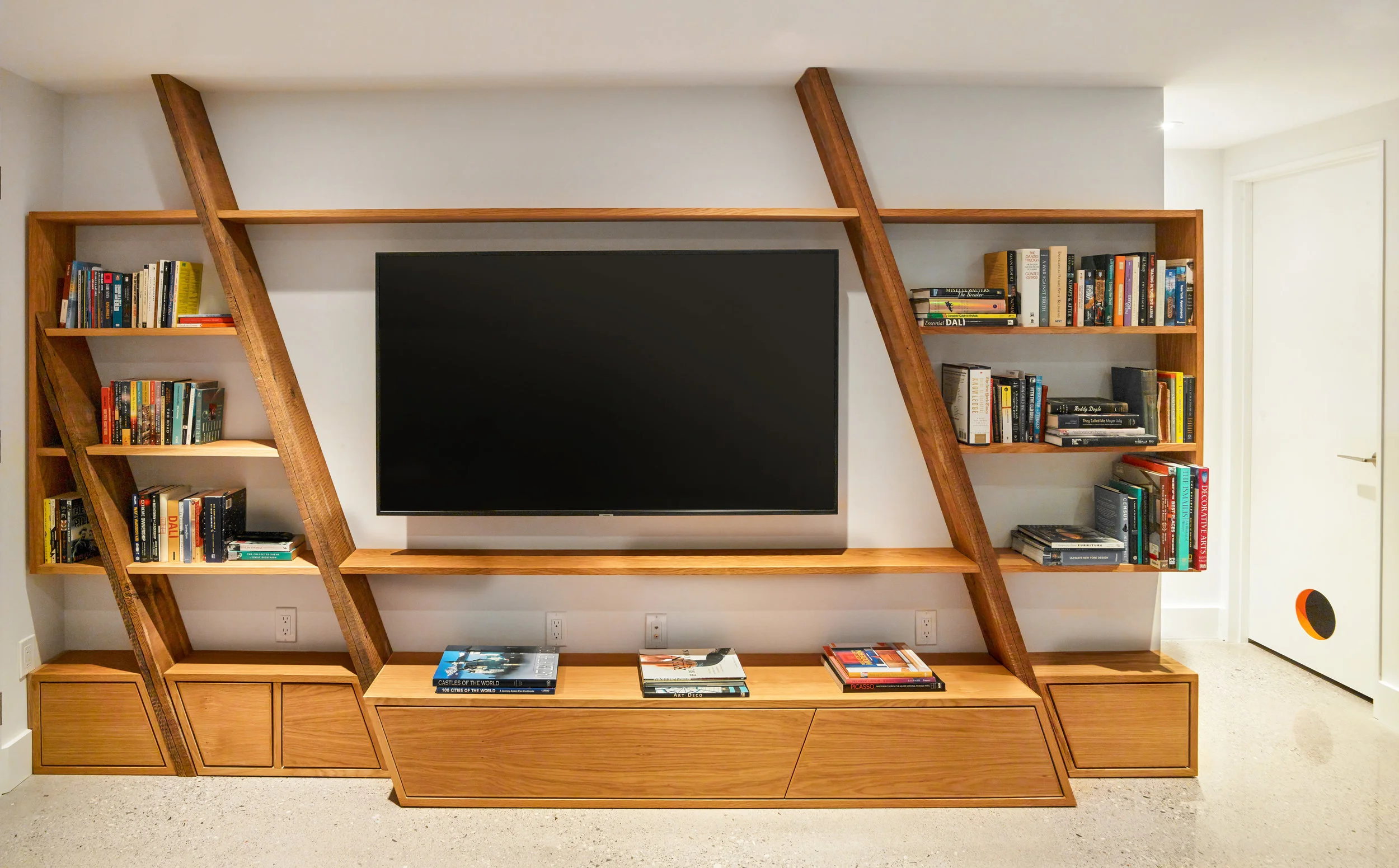 In the basement, a custom built in shelving unit uses rough, reclaimed wood to house a collection of books around the TV - a casual lounge space for movie watching and sleepovers.