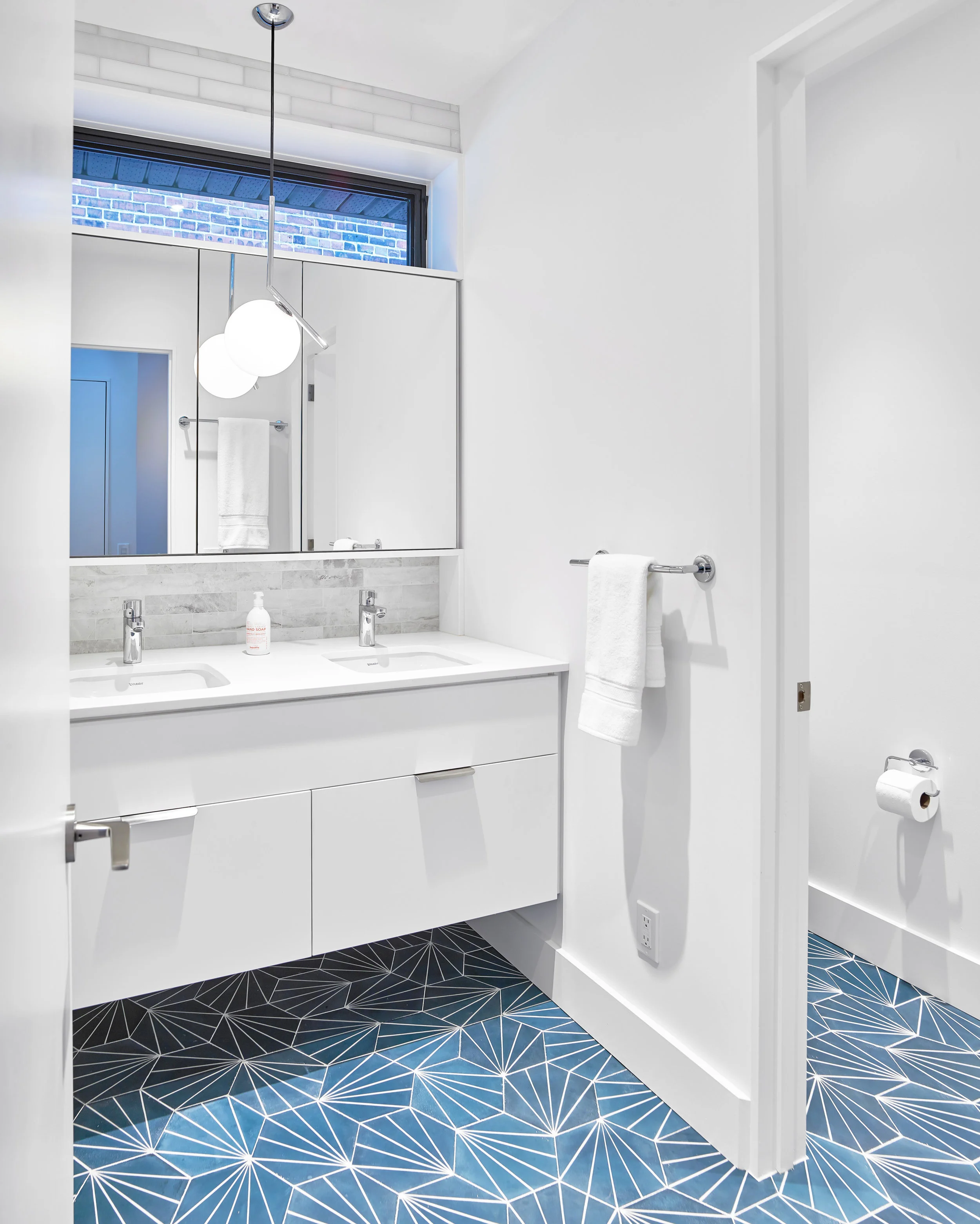 A clean palette for bathroom is enriched by a bold patterned floor tile. Since the bathroom is shared by the family it includes a separate toilet room and double vanity to enable it to be used by more than one person at a time.