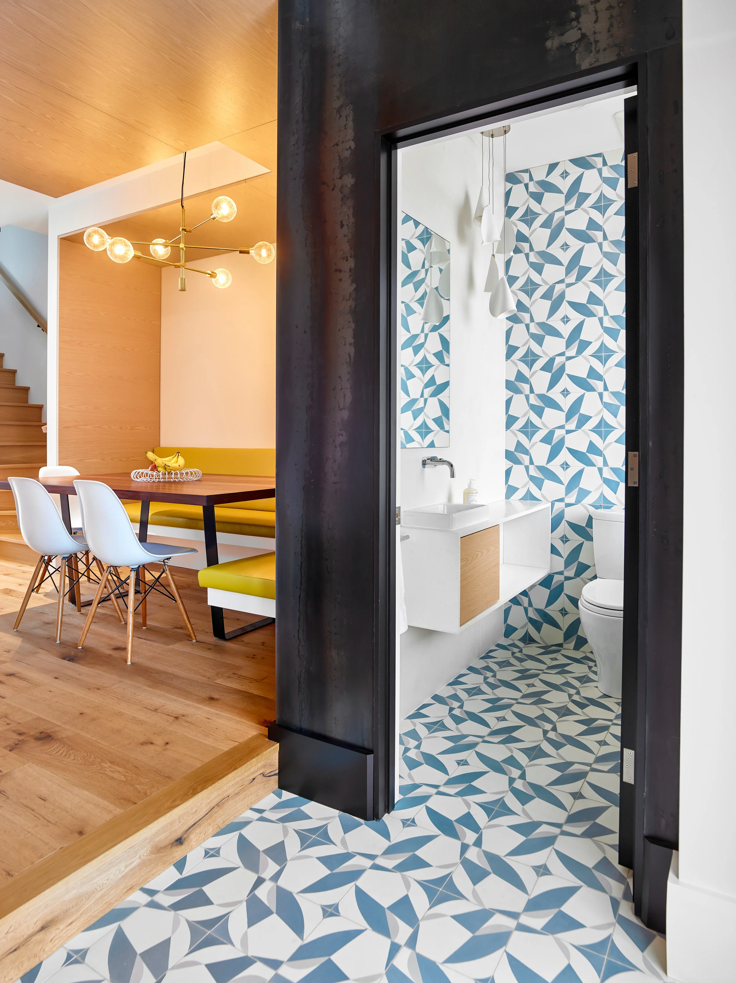 Stepping up from the entryway, the ground floor opens onto a cozy built-in banquette with a wood ceiling that wraps down one wall, defining a warm space for gathering and enjoying meals together.
