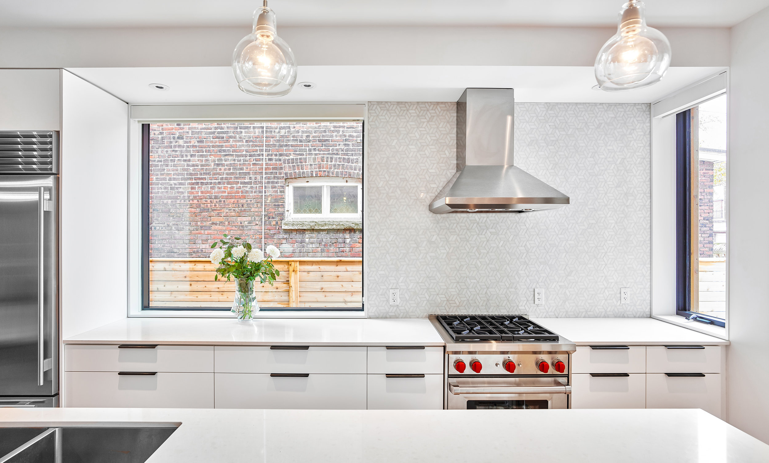 In contrast, a clean white kitchen is located in the heart of the home. The house takes full advantage of a unusually wide side yard by punching large windows in the side wall, which is typically not allowed on most Toronto lots where homes are closer together. The bright, white kitchen injects light deep into the middle of the house, instead of relying only on the front and rear walls as the preliminary sources of daylight.