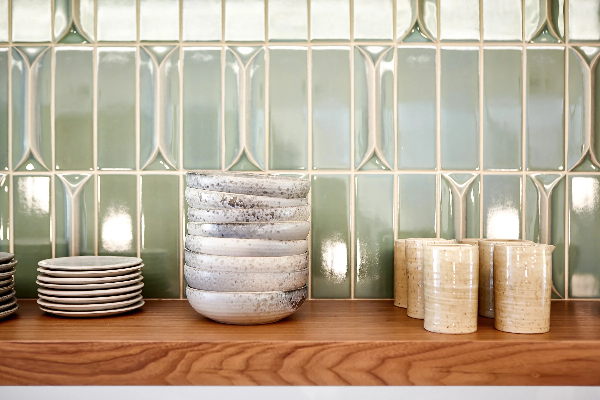 A floating walnut shelf runs the length of the kitchen, providing the perfect spot for the couple’s collection of beautifully curated tableware, set against a wall covered in light green, glazed ceramic tile. A number of sculpted, three-dimensional