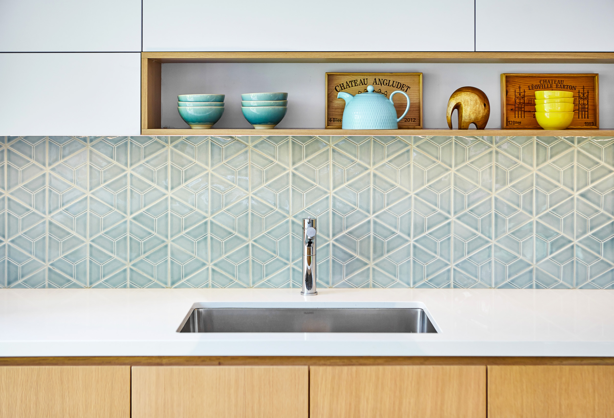 A crisp, clean palette of white and light wood cabinetry is enriched by a handmade backsplash tile with natural variations in the glaze that brings an softness to the space.