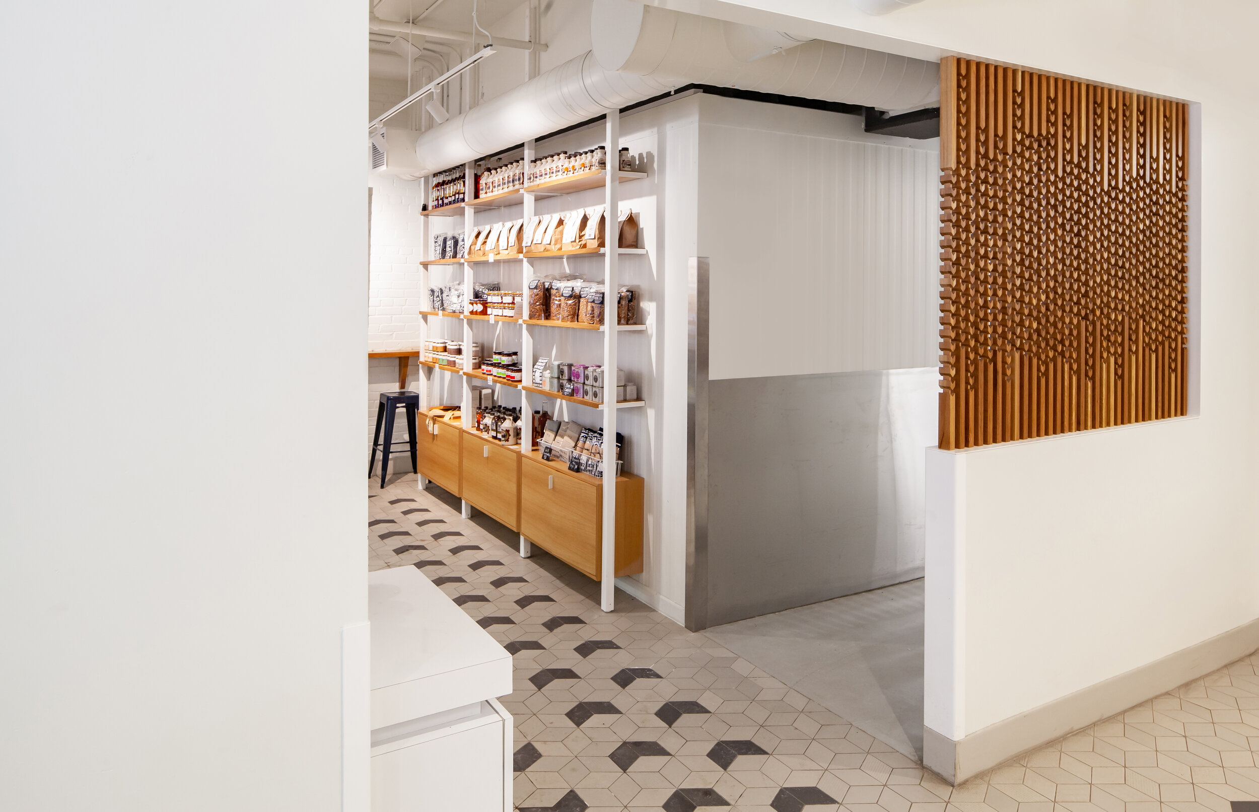 The simplicity and rigour at the core of the baking process are reflected in subtle details throughout the space. A wood screen and patterned tile floor reference the shapes and patterns of a wheat field with a simplified geometric motif.