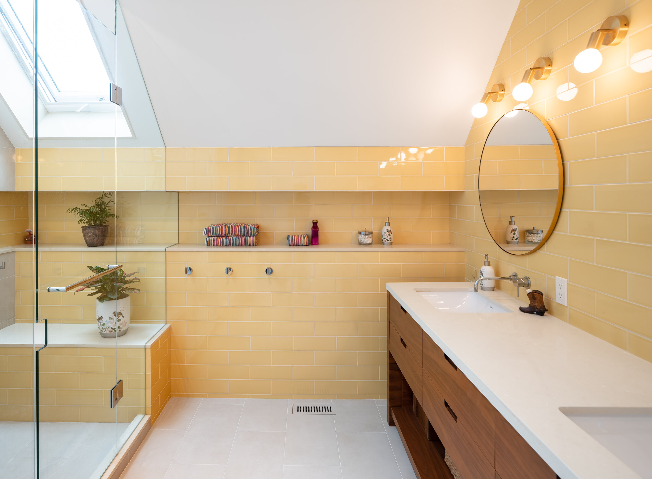 A delicate, handmade yellow glazed tile creates a warm, spa-like feel in the third floor main ensuite. The yellow tile stretches the entire width of the room within a niche to link the shower and the vanity walls, and provides an accessible ledge f
