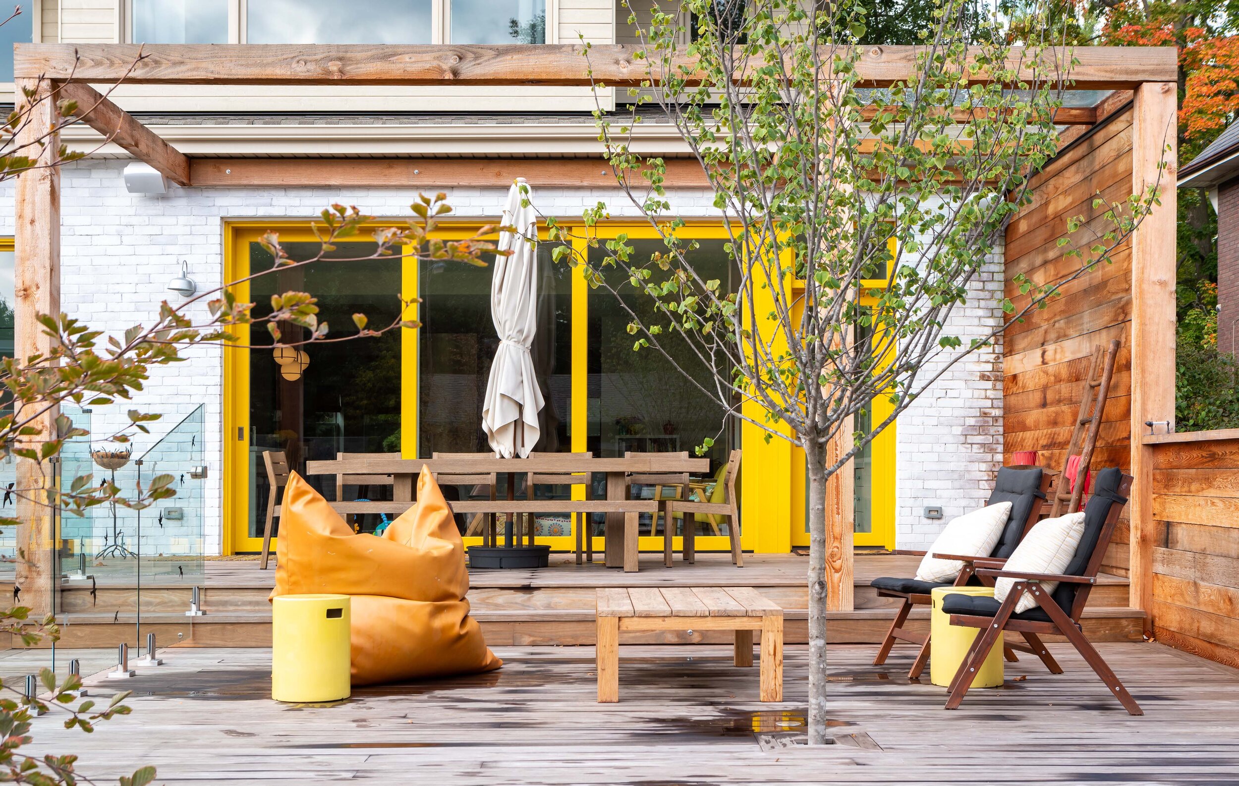 The whitewashed brick addition is punched with vibrant yellow windows and doors. A pergola over the raised deck helps mediate the transition between inside and out, creating an in-between zone with shaded views over the yard and pool.