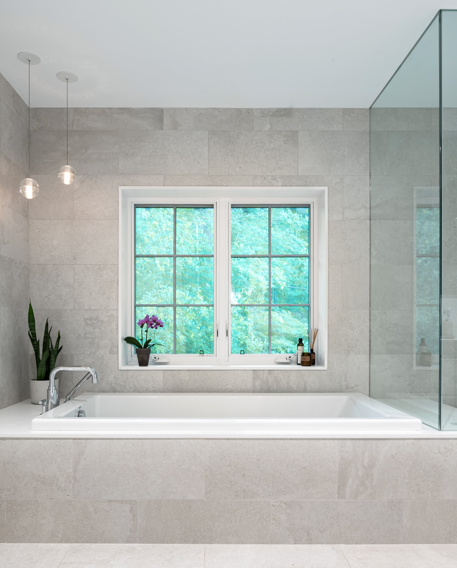 The master ensuite features a generously sized built-in tub as well as a steam shower. The neutral palette allows the view of the trees outside to be the main focal point, and pop of colour.