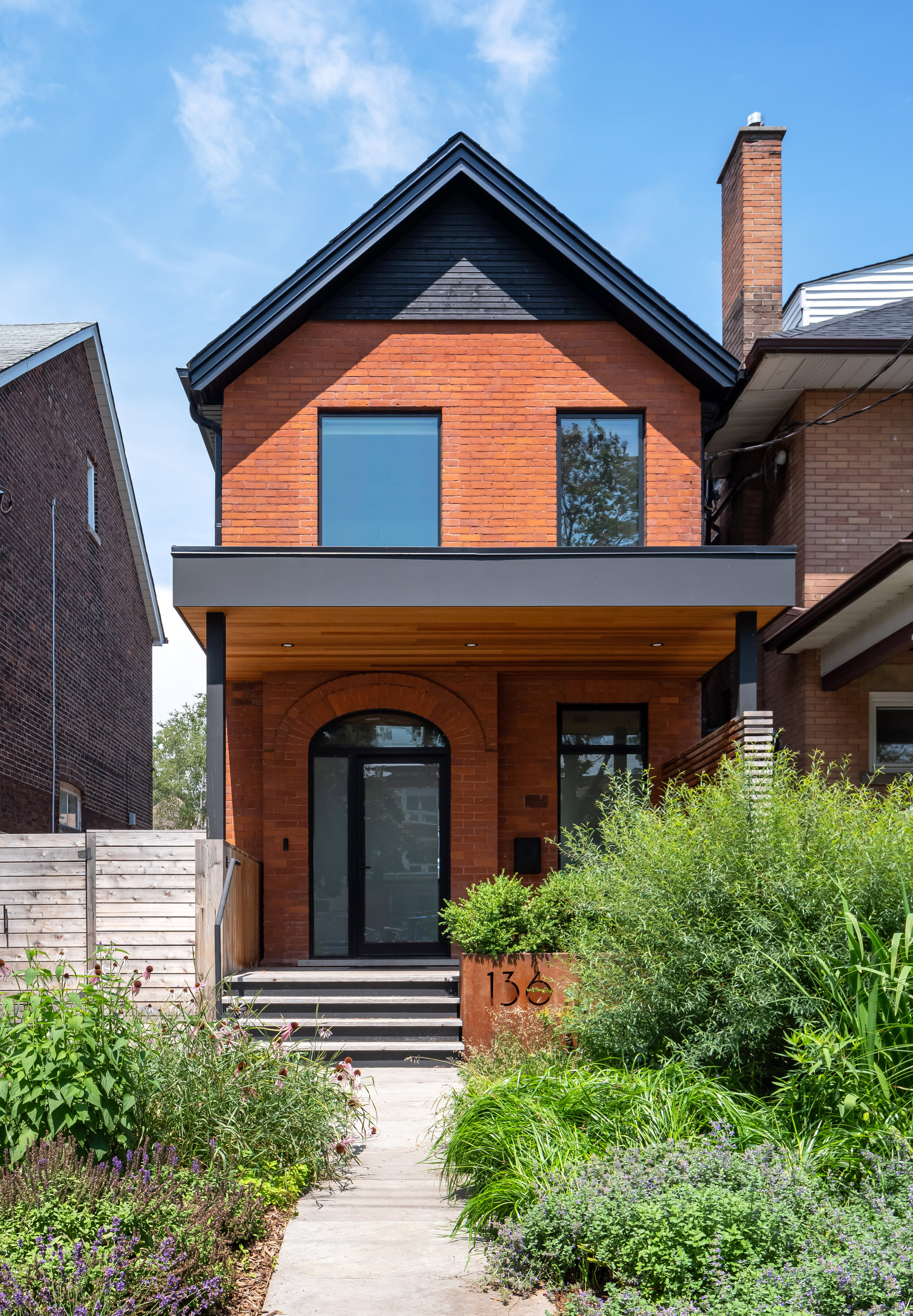 The front facade is completely reimagined to give the home a fresh presence on the street. The front door is cleverly relocated from a nondescript opening on the right to be celebrated within a larger arched opening on the left. An old porch is rep