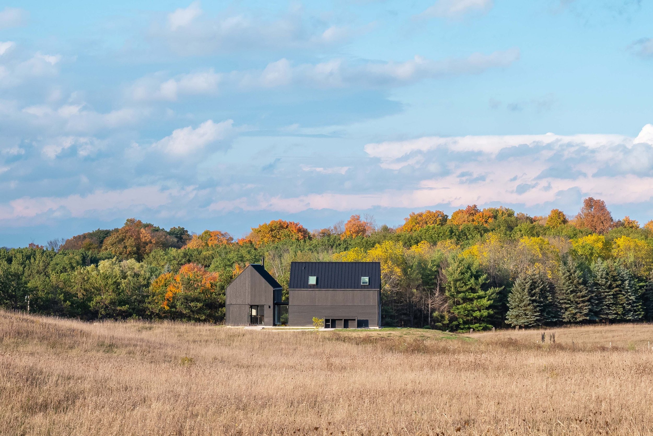 The home is composed of two main sculptural volumes nestled into the surrounding wheat fields. The house was carefully oriented to prioritize views out to the forest beyond, and to allow for optimal light inside. The landscape changes dramatically