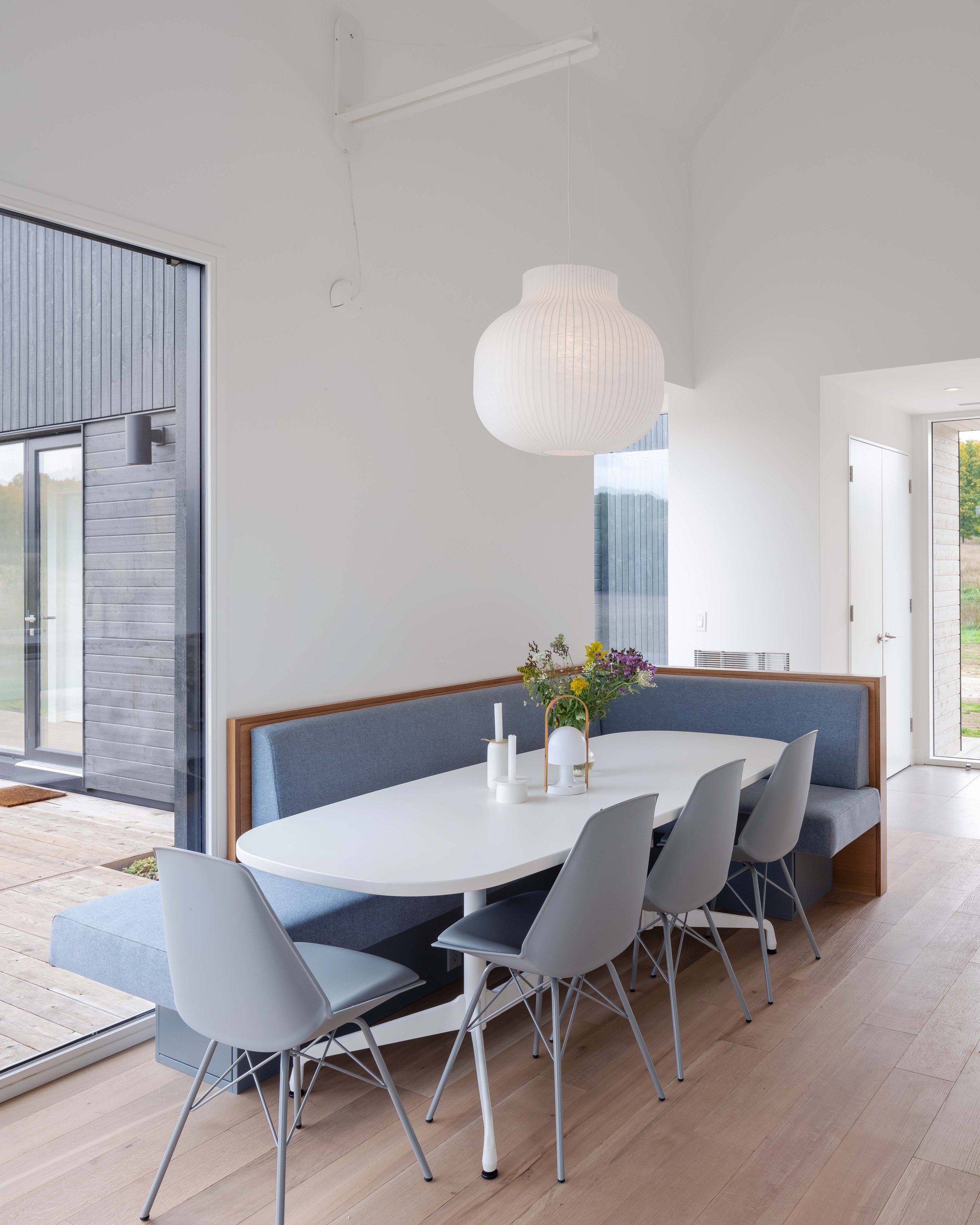 A built-in banquette in the dining area provides ample seating for the large family, as well as a touch of colour and texture. A large Muuto Strand pendant light is suspended on an arm over the table and provides a warm, ambient glow.