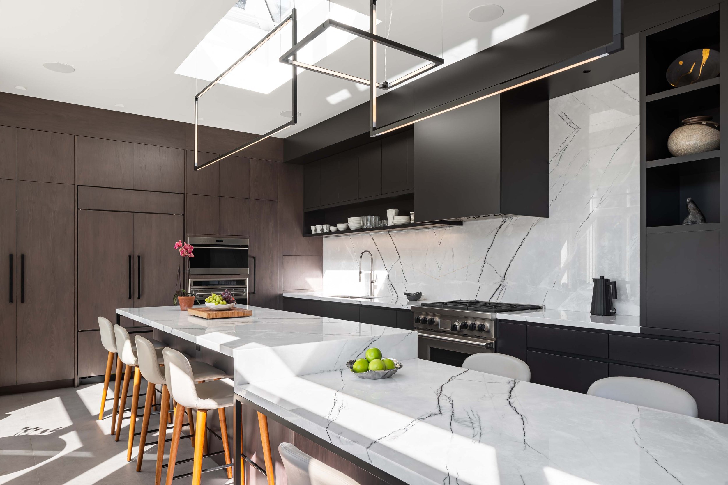 The marble in the kitchen is treated, and lit, as if it were a piece of art. The large backsplash is framed by the contrasting black millwork. A custom composition of sculptural rectilinear lights appears to float in the air above.