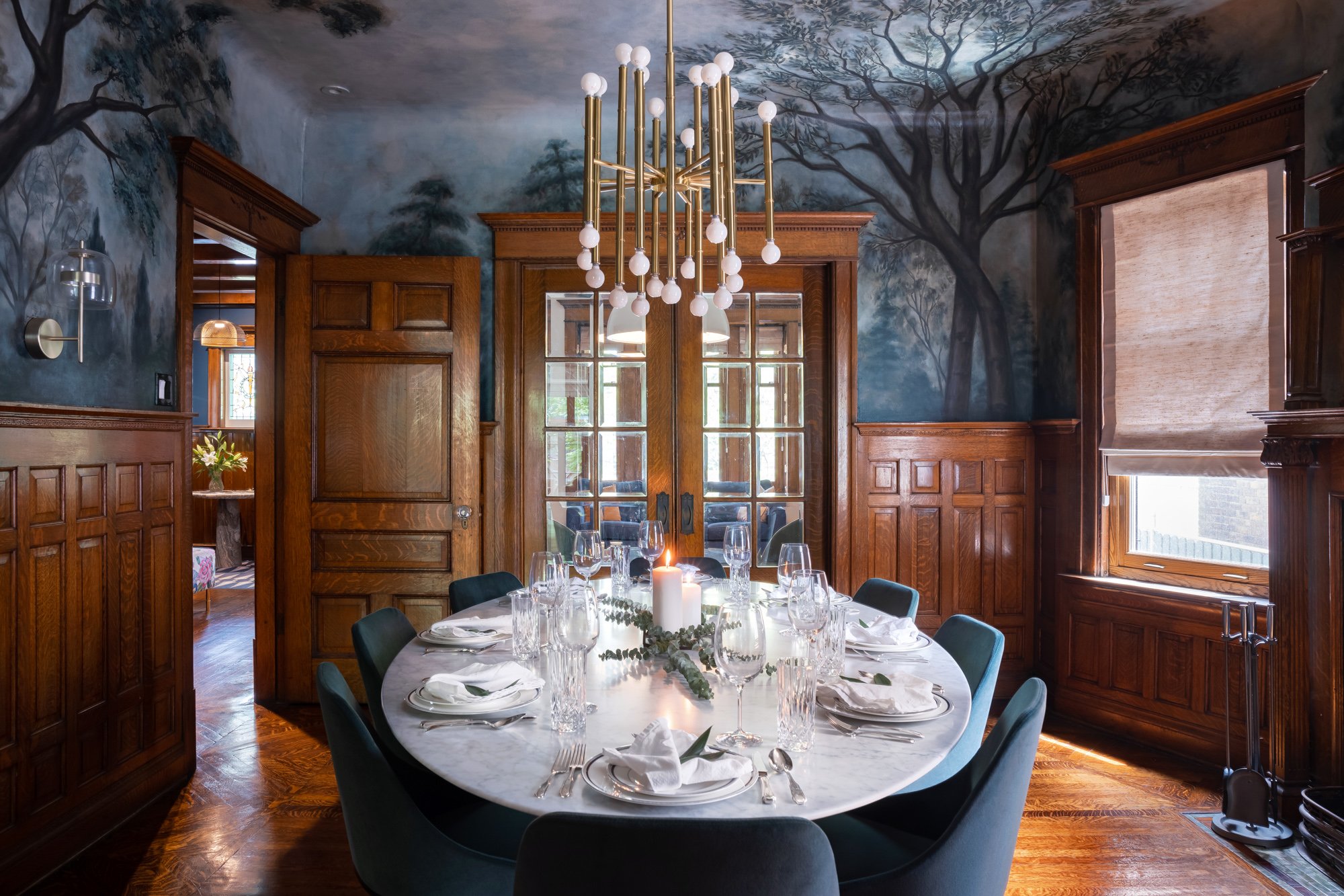 A custom, hand-painted mural by local artists surrounds the entirety of the dining room and creates a space that feels dramatic and moody, while still feeling like an elegant and formal dining space.