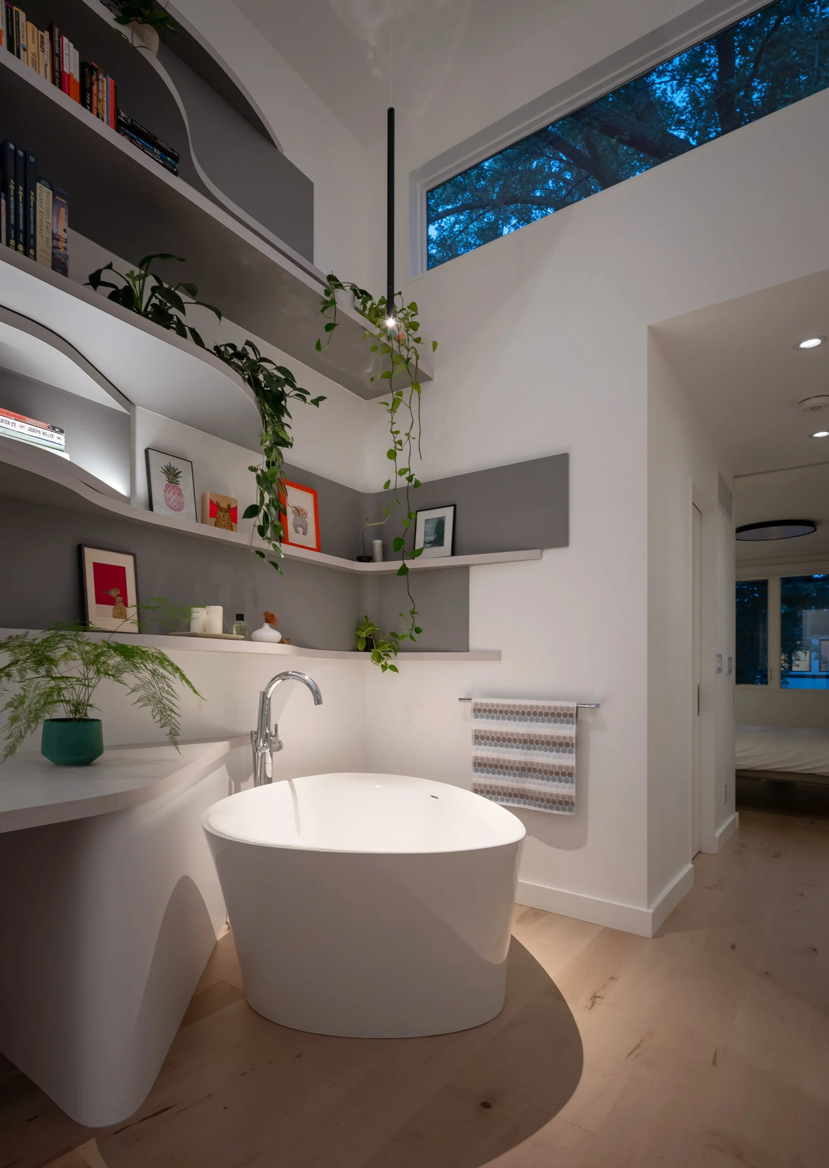 At night, the tub is spot lit by a pendant light, and the ambient glow of the bookshelf lighting, creating a soothing ambiance for relaxing in the bath at the end of the day.