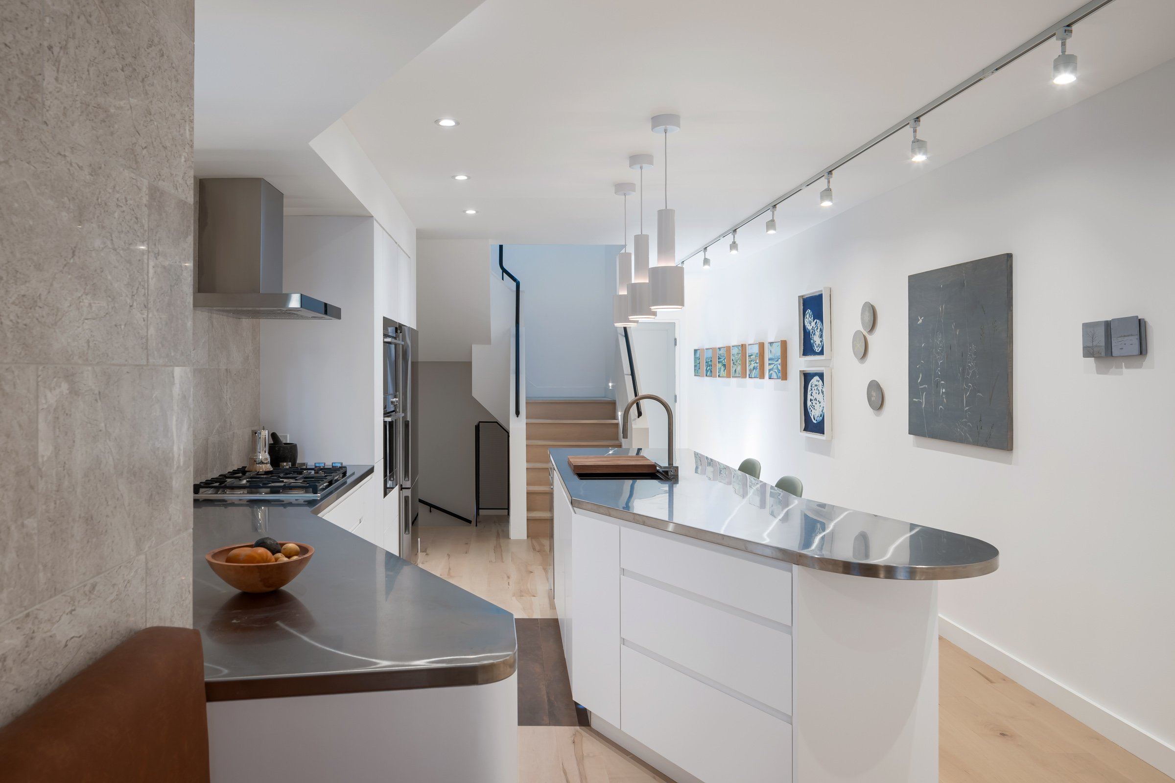 The ground floor is also entirely open concept, with carefully defined living spaces that unfold in sequence as you move deeper into the house. A continuous bank of millwork flows along the south wall of the whole floor, transforming from a kitchen,