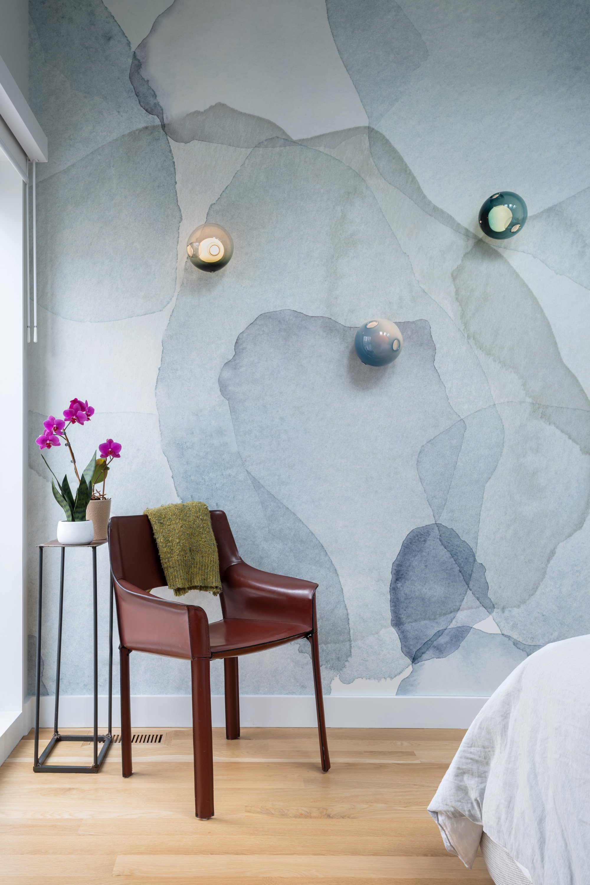 Custom wallpaper in the bedroom features a flower petal design that echoes the blossom of the cherry tree outside when in bloom. The palette is watery and soft, creating a serene place to start and end the day. Bocci sconces float across the wallpap