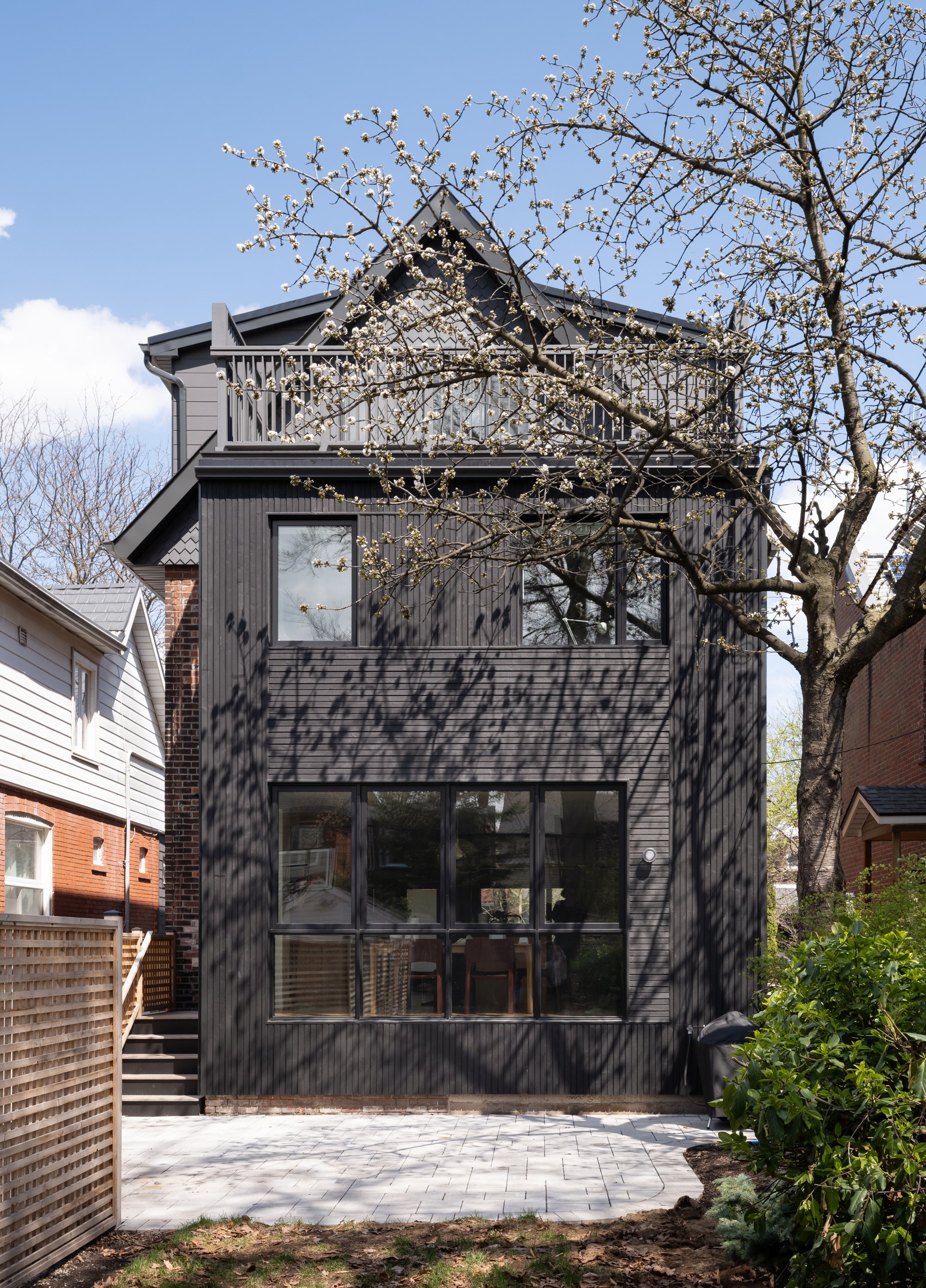 An existing small single storey addition at the rear was demolished and replaced with a two-storey addition with a roof deck on top. The addition was clad in black Cape Cod wood siding. Directional changes in the cladding between windows provides su