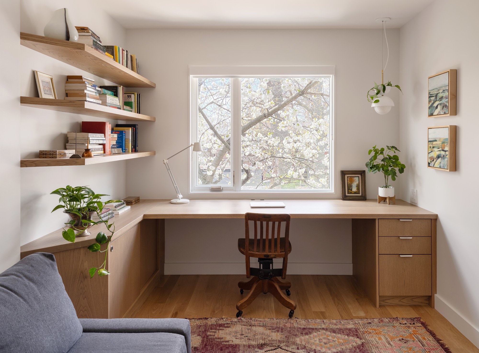 On the second floor, the main office space takes advantage of beautiful west light. In the spring, the cherry tree outside bursts into bloom, creating a soft, ethereal view. Faceted floating shelves and a built-in desk provide storage and negotiate