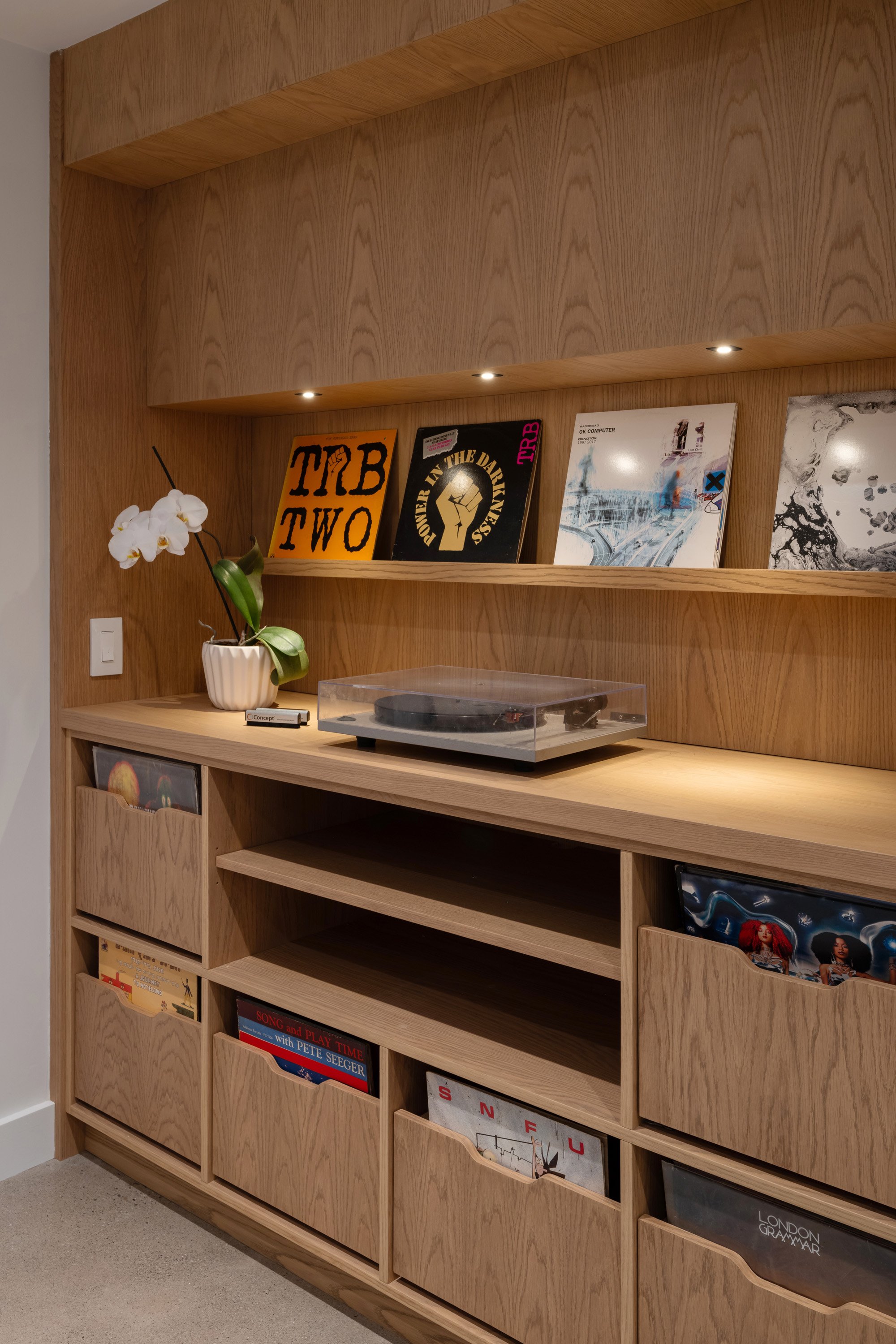 In the basement, a custom piece of millwork houses the record player and extensive vinyl collection. The structure for the side door landing is concealed in the millwork by an illuminated display ledge for album covers.
