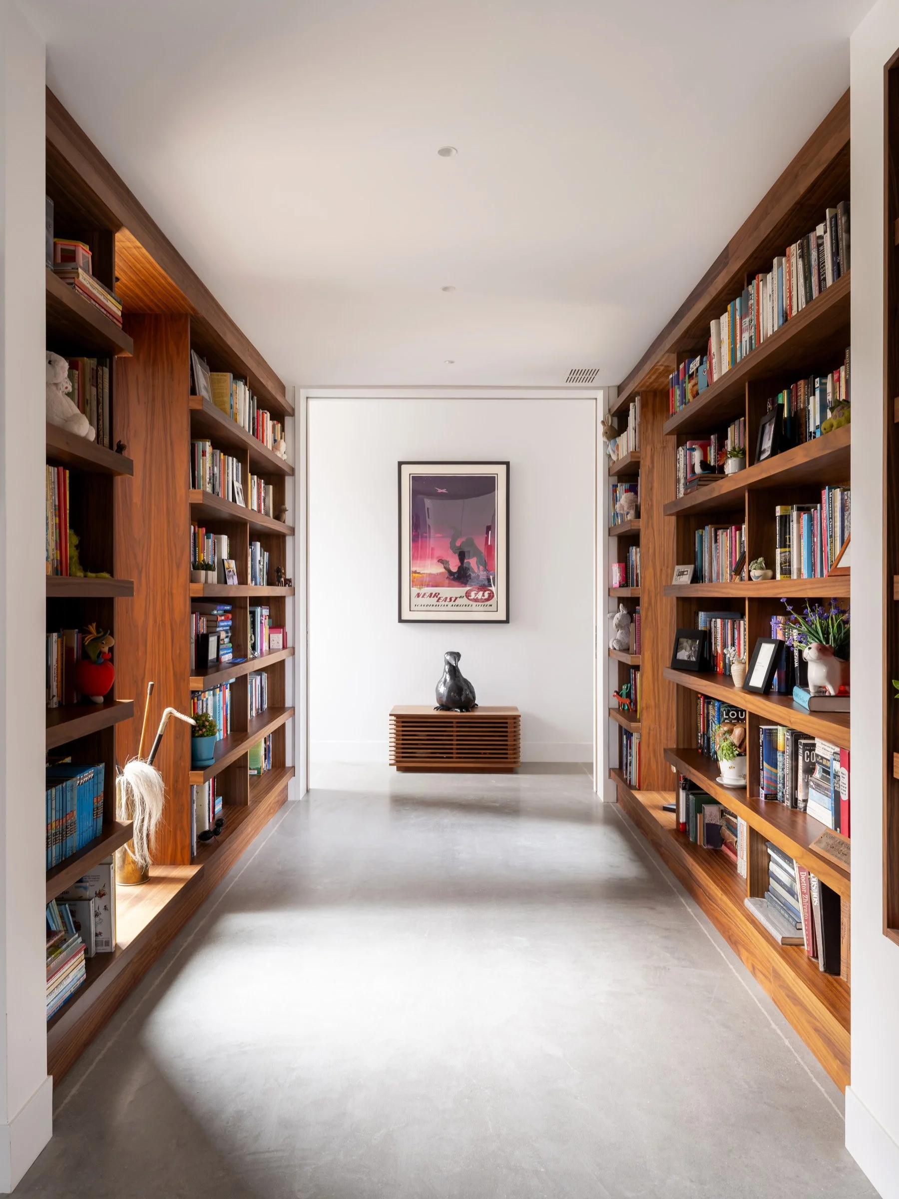  Connecting the living areas to the primary bedroom suite is one of two single story hallways that separate the private and more public areas of the home. The hallway is lined with floor-to-ceiling custom bookshelves which offer display space for the
