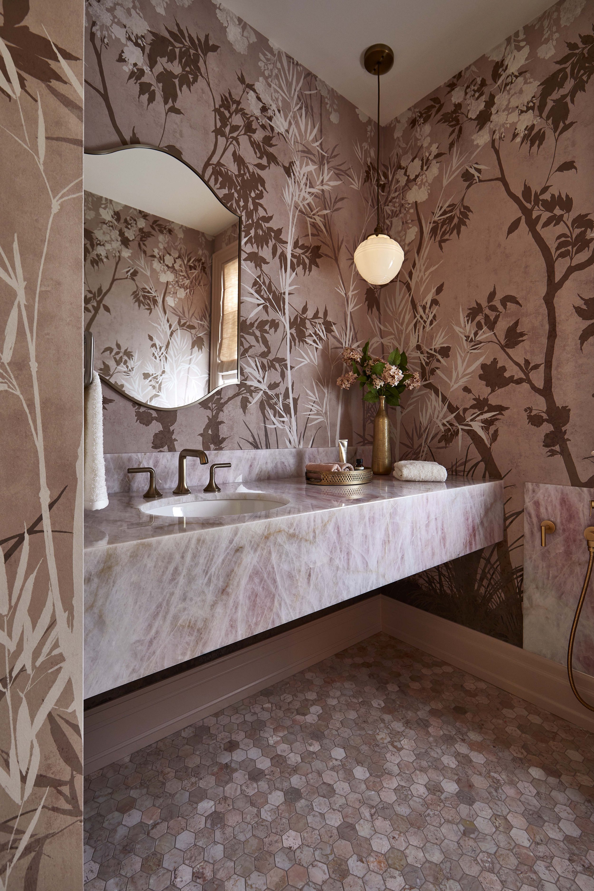  Located off the mudroom, this powder room is a jewel box of luxurious pink marble, natural quartz, and mural wallpaper. 