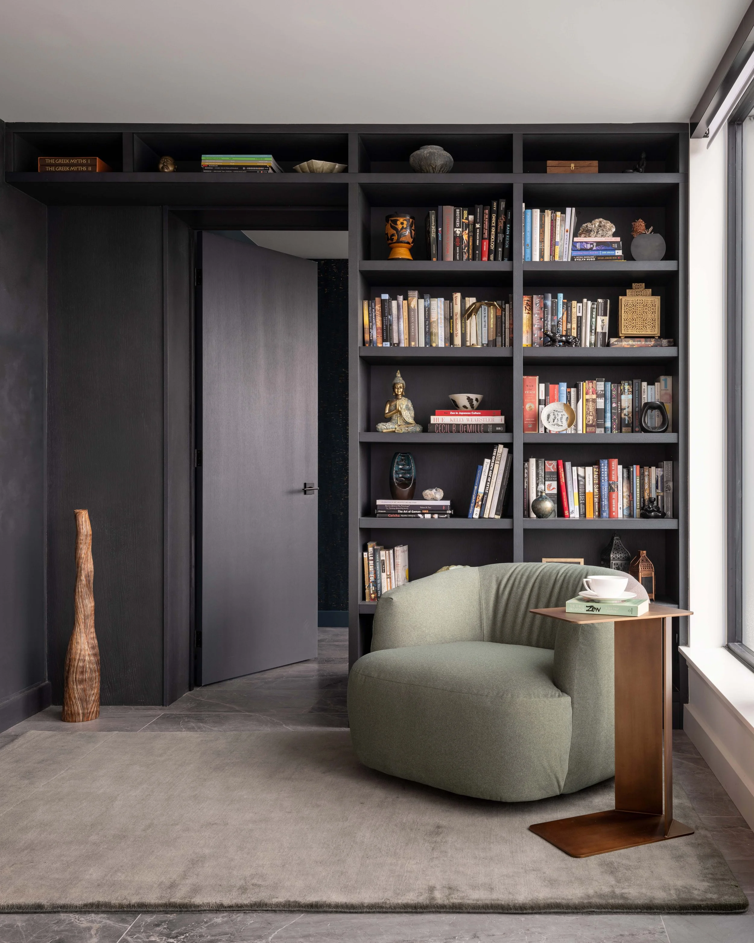  A reading nook with a view on to the terrace is nestled beside floor-to-ceiling built-in bookcases surrounding the door to the primary suite. 