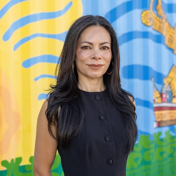 Photo of Mariana. She has long dark hair and is wearing a white shirt and gold earrings