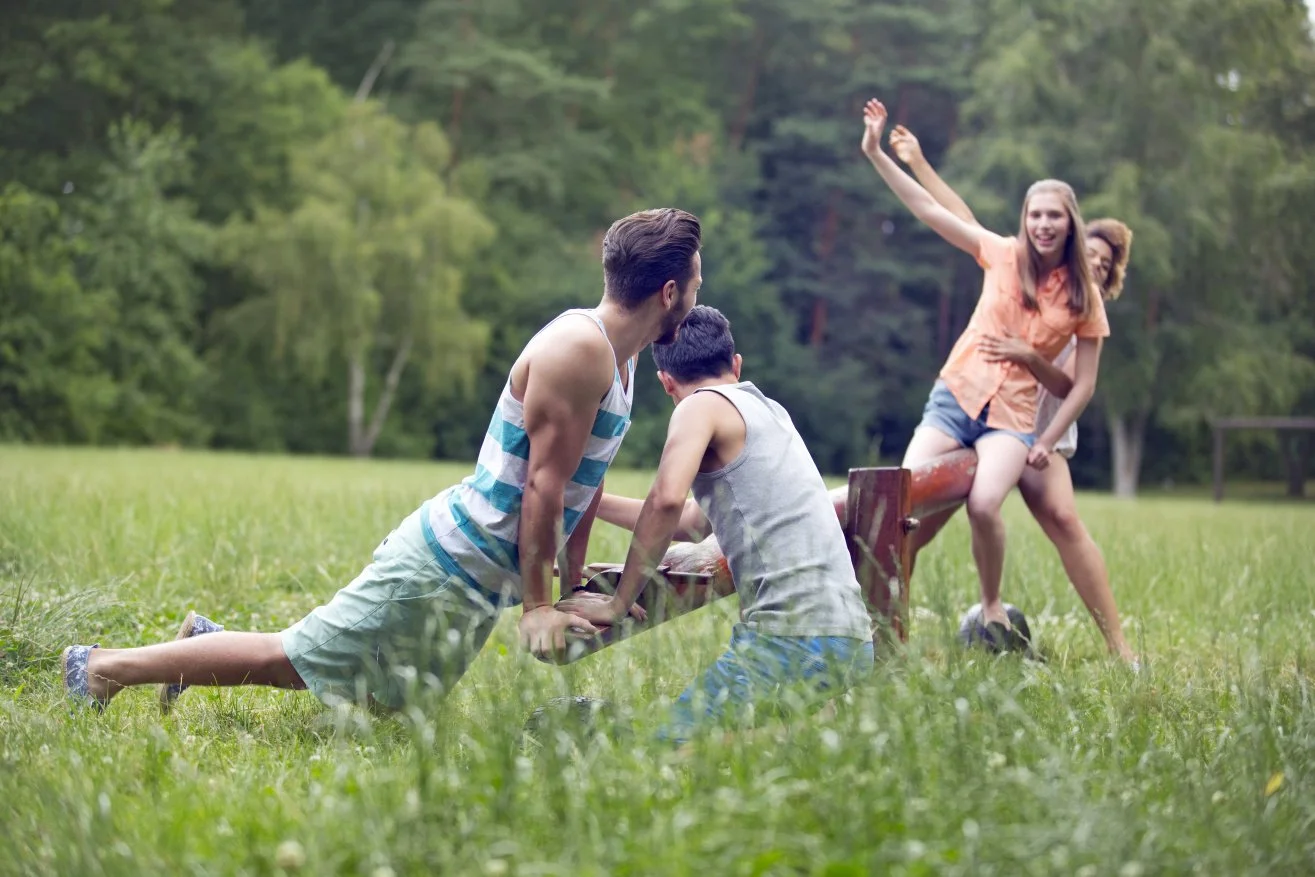 Teenagers playing on a seesaw on a green lawn.