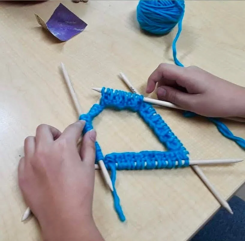 An image of a child's hands holding knitting needles with blue yarn.