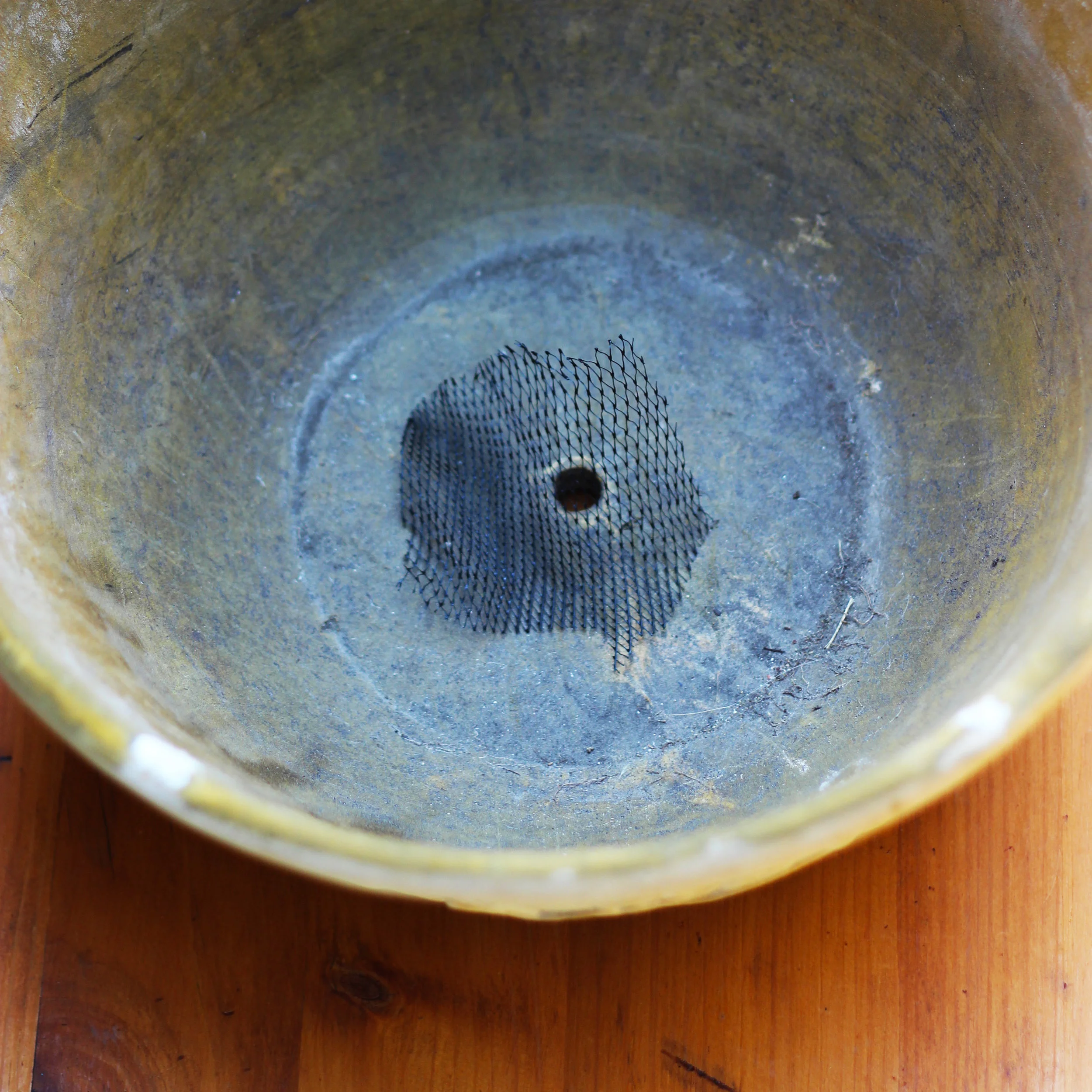 Cut a 2.5 x 2.5 inch piece of netting or screen and put over the hole so soil doesn't come out.