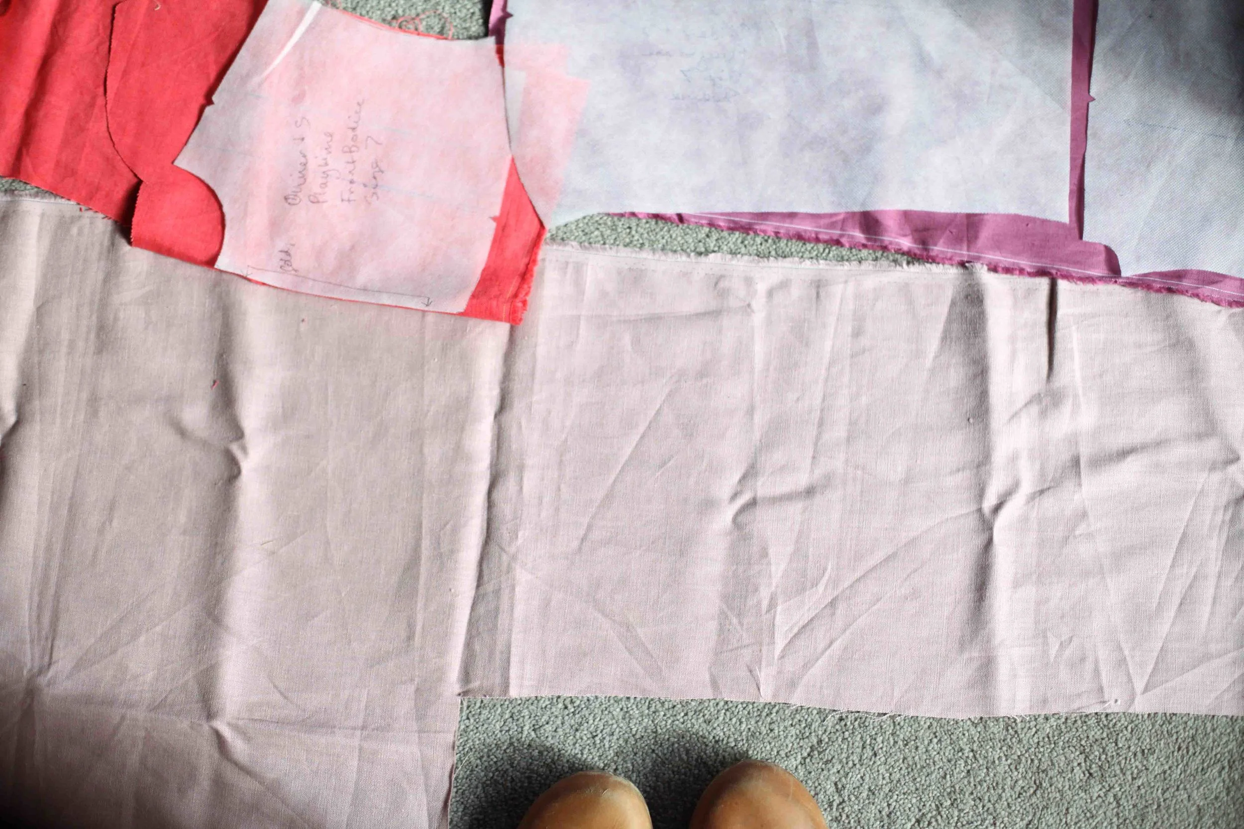 A photo of me trying to get all the pattern pieces to fit onto my scraps to make a scrap dress. You can see what the front turned out like below. One sleeve of the frock will be the light pink and the other the dark pink.