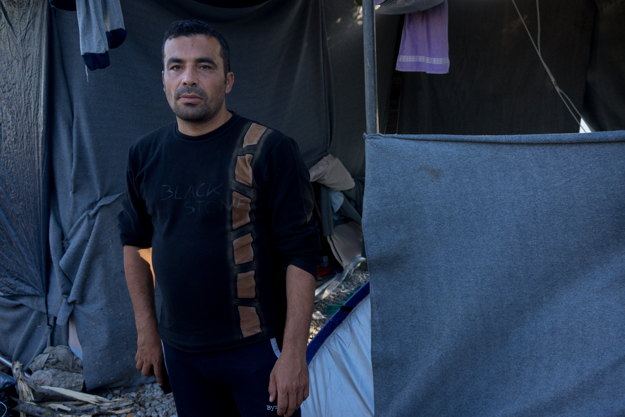 October 19, 2017. Moria camp, Lesbos, Greece. Aarif poses for a photograph in front of their camp site outside Moria hotspot. Aarif used to work in the army in Syria, when he left the army he was kidnapped and tortured by ISIS for a year before he managed to escape. He arrived in Greece in July, he expressed how lowly and humiliated he felt. In November he went back to Syria. 