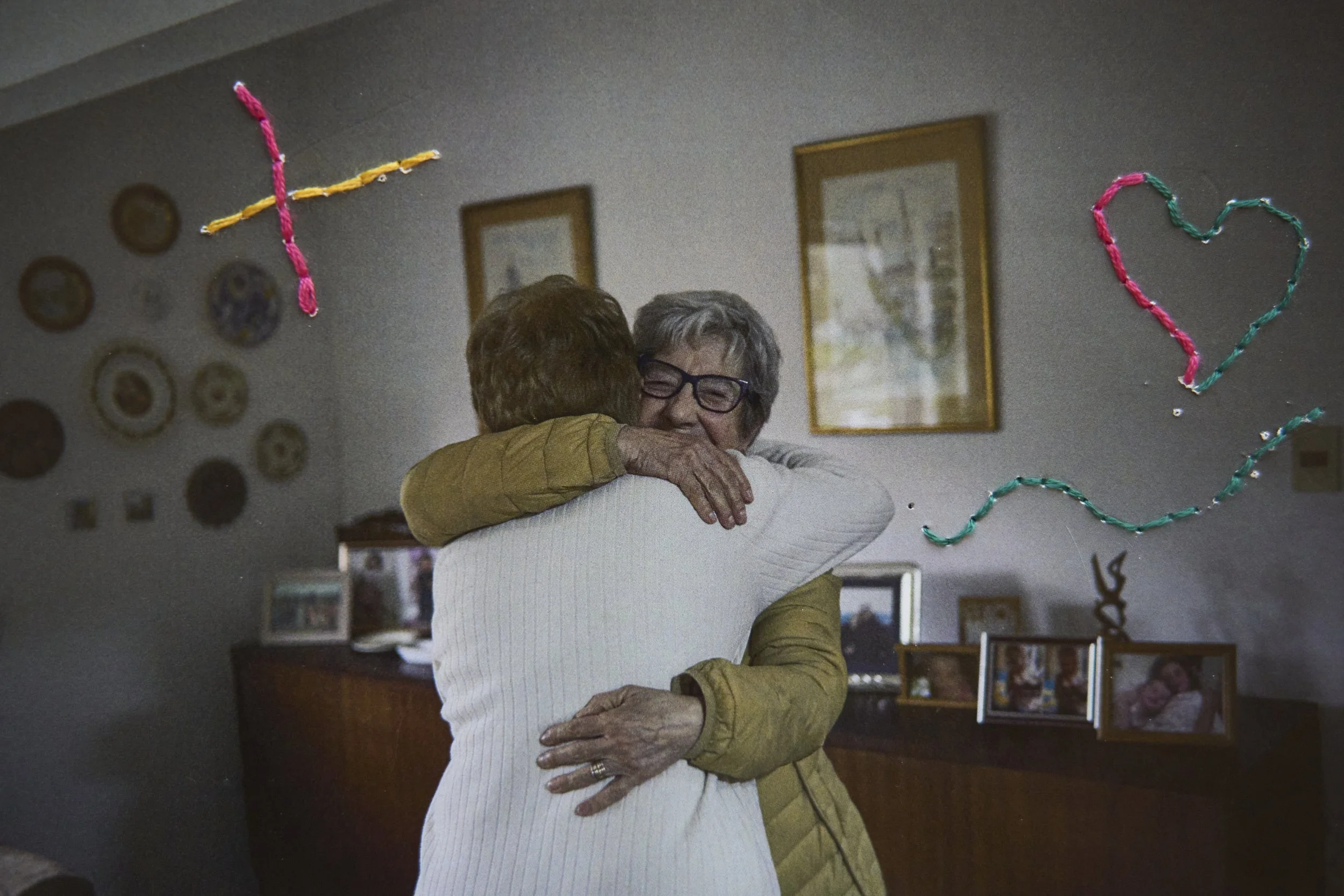  Neighbors and friends Beatriz and Lucia hug in Lucia's home, after an afternoon spent together. Embroidery by Sara 