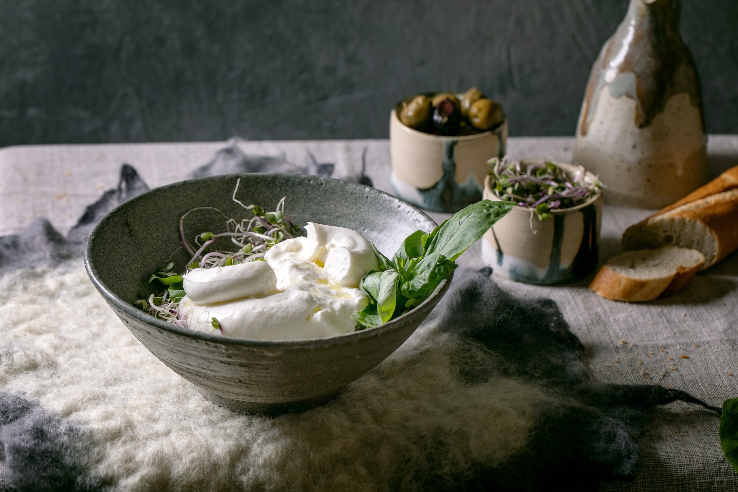 traditional-italian-burrata-knotted-cheese-salad-grey-ceramic-bowl-table-with-felted-napkin-sliced-bread-olives-green-sprouts-around-healthy-mediterranean-dinner.jpg