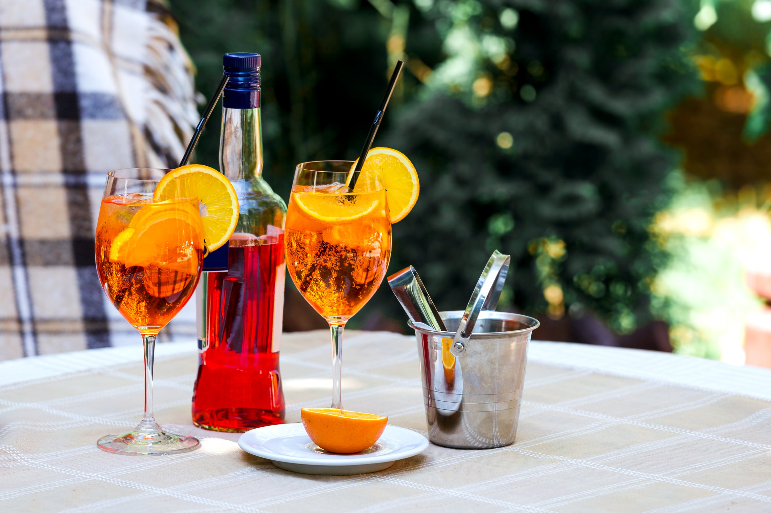 aperol-spritz-cocktail-glass-plaid-table-leaves-sun-orange-ice-bucket-shadow-sunlight.jpg